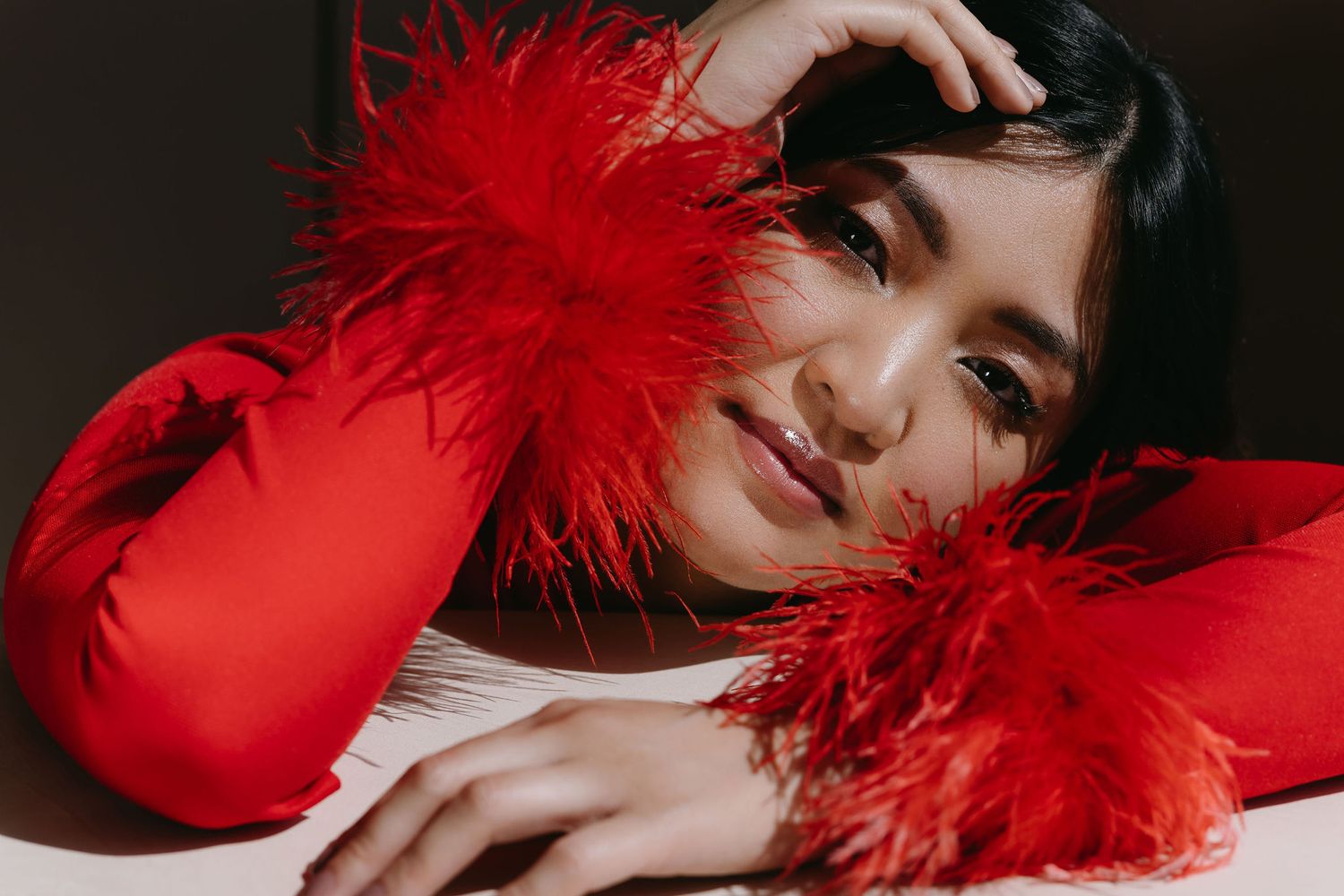 Artistic portrait with vibrant red feather details and matching sweater in dramatic lighting.
