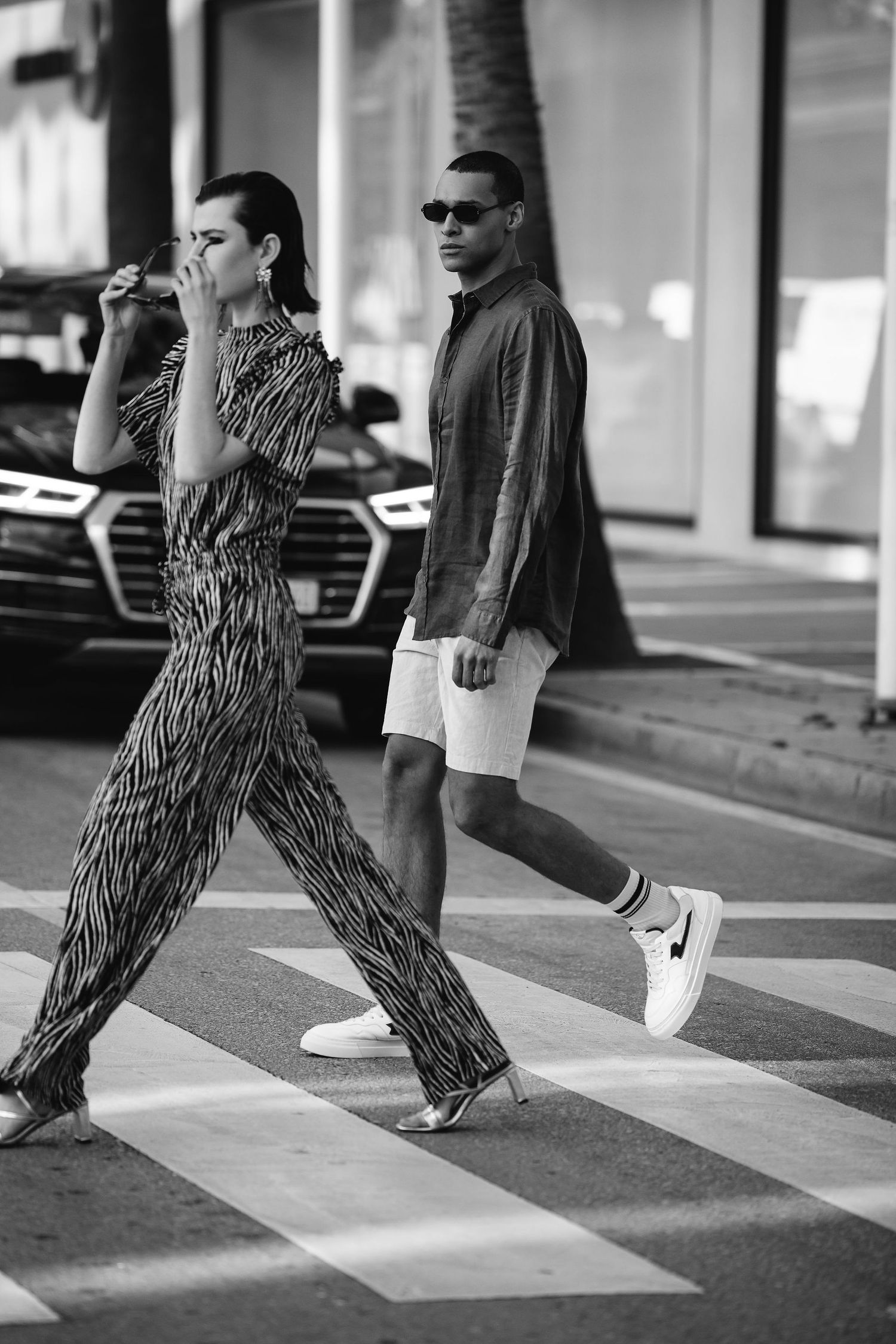 Black and white street photo of two people crossing a zebra crossing in stylish outfits.