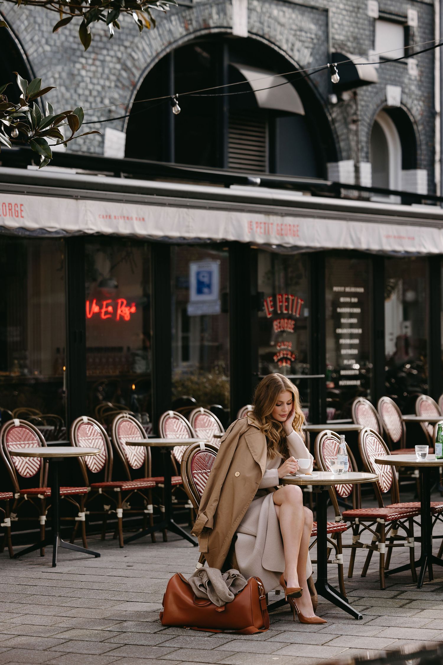 Atmospheric scene at a Parisian cafe with bistro chairs and someone sitting with a leather bag.