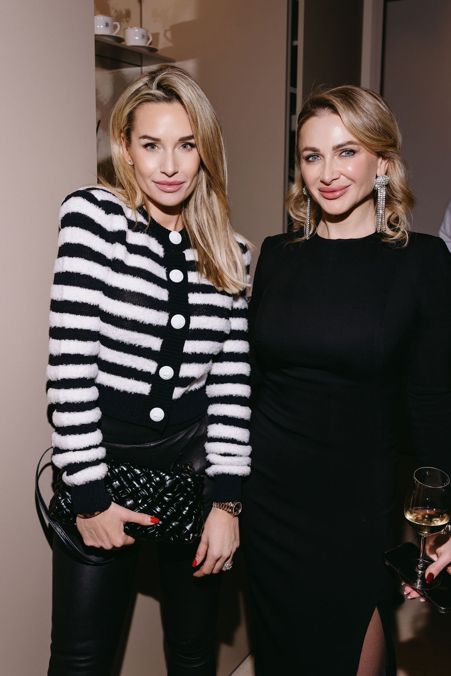 Two women posing at event wearing contrasting black and striped outfits.