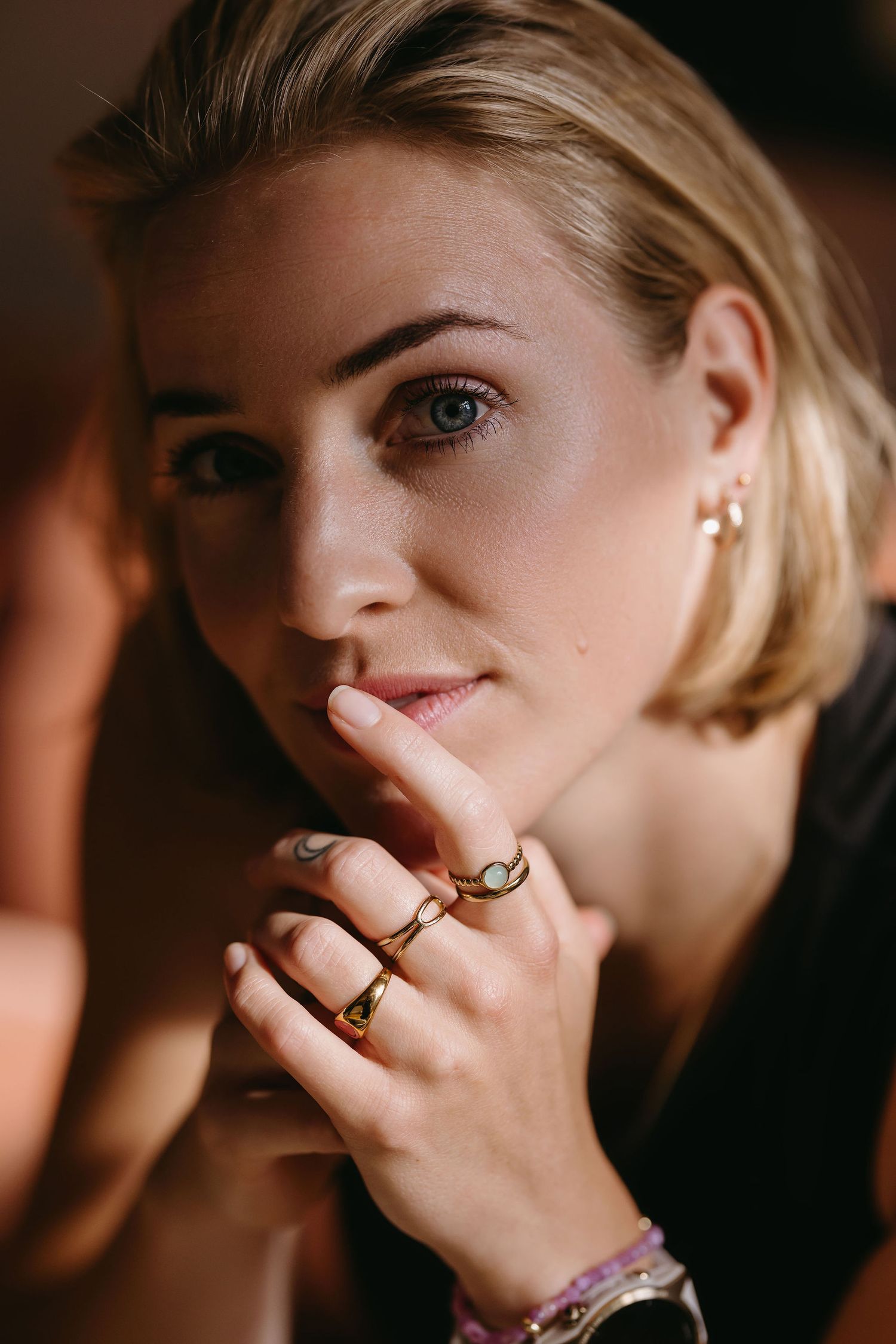 Close-up portrait showcasing multiple rings and natural makeup look.