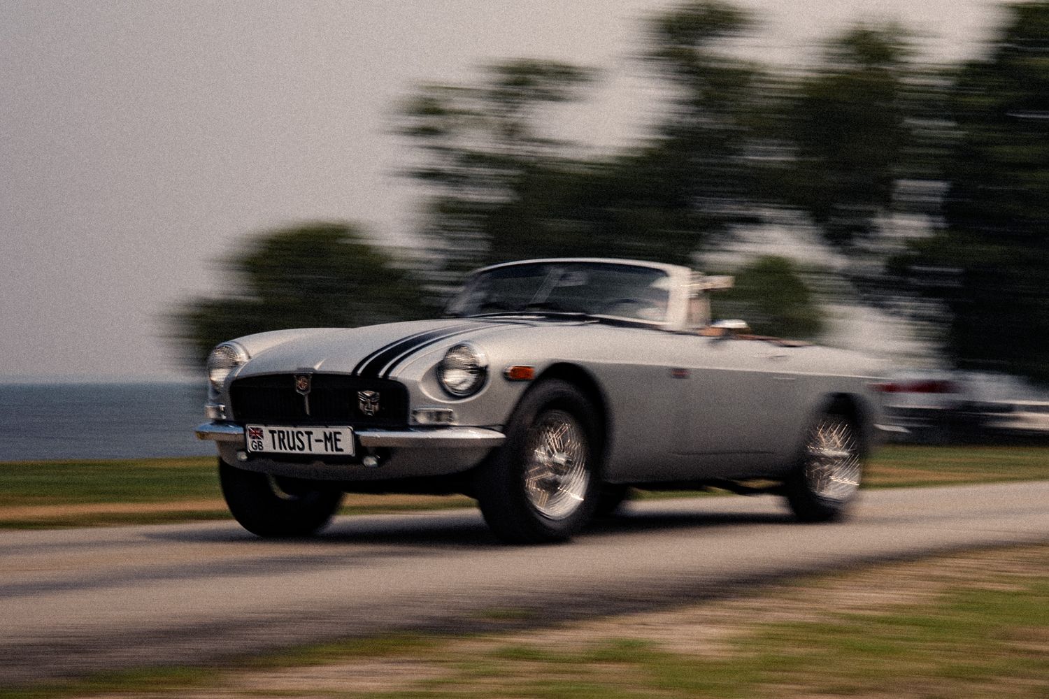 A classic silver convertible sports car speeds along a coastal road, showcasing vintage style and elegance.