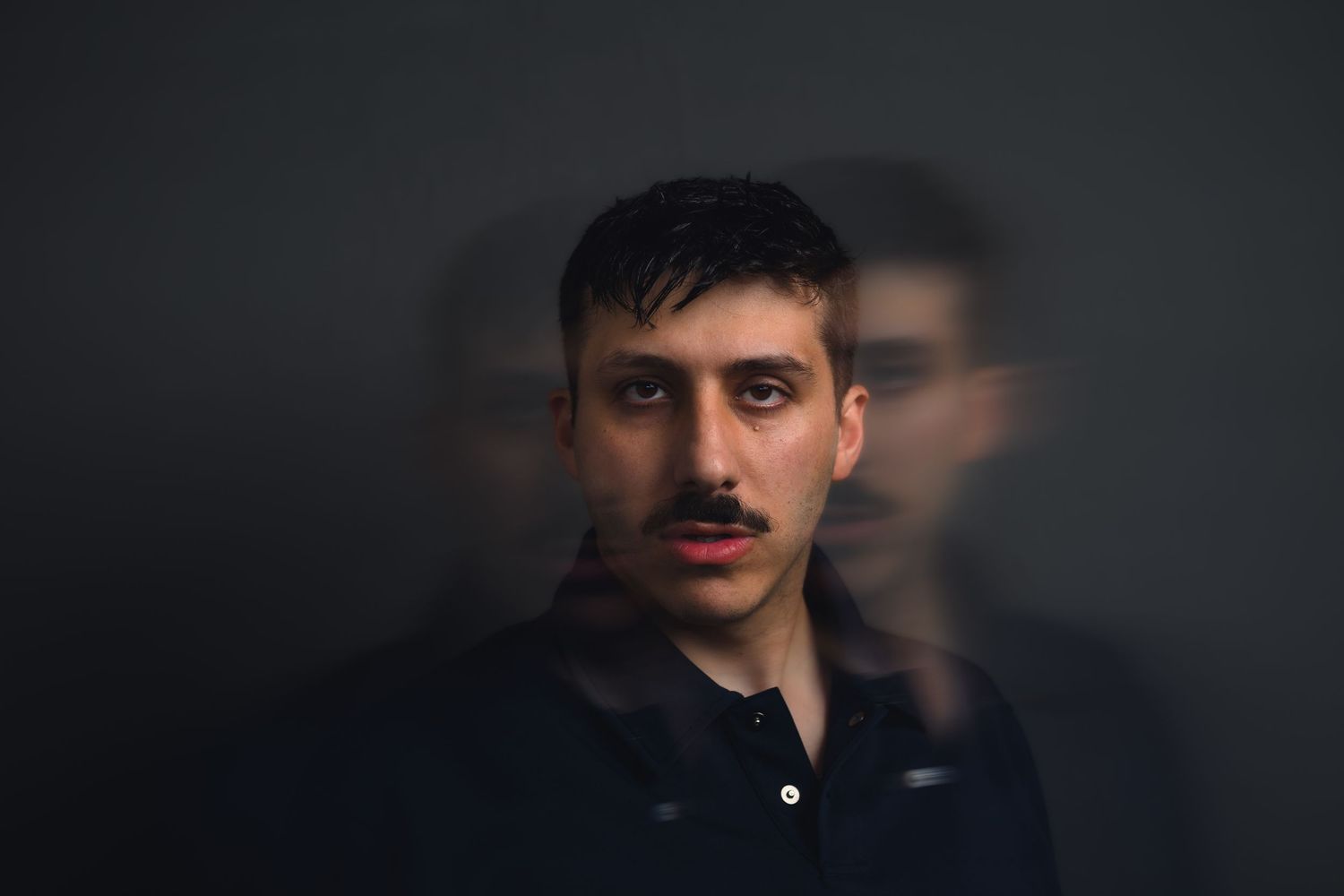 Young man with mustache in artistic motion-blur portrait against dark background.