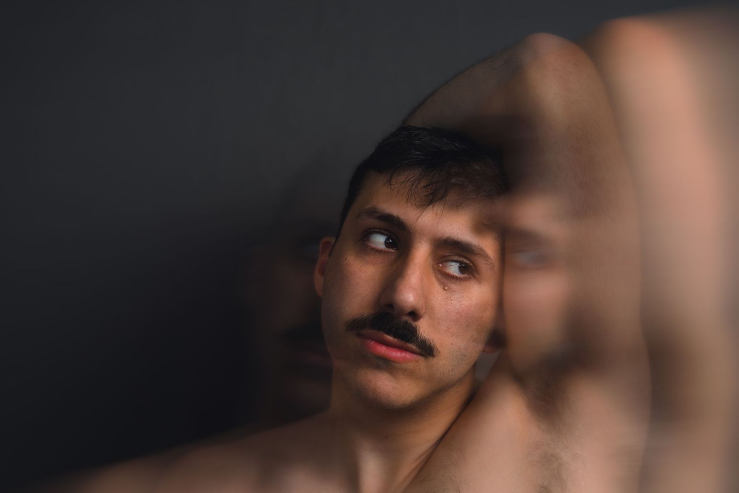 Color portrait of a mustachioed young man looking sideways, captured with a creative fragmented mirror reflection.