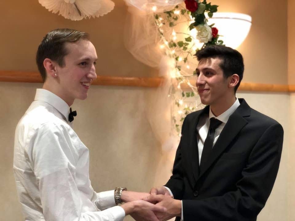 Two grooms holding hands and smiling at each other during their wedding ceremony.