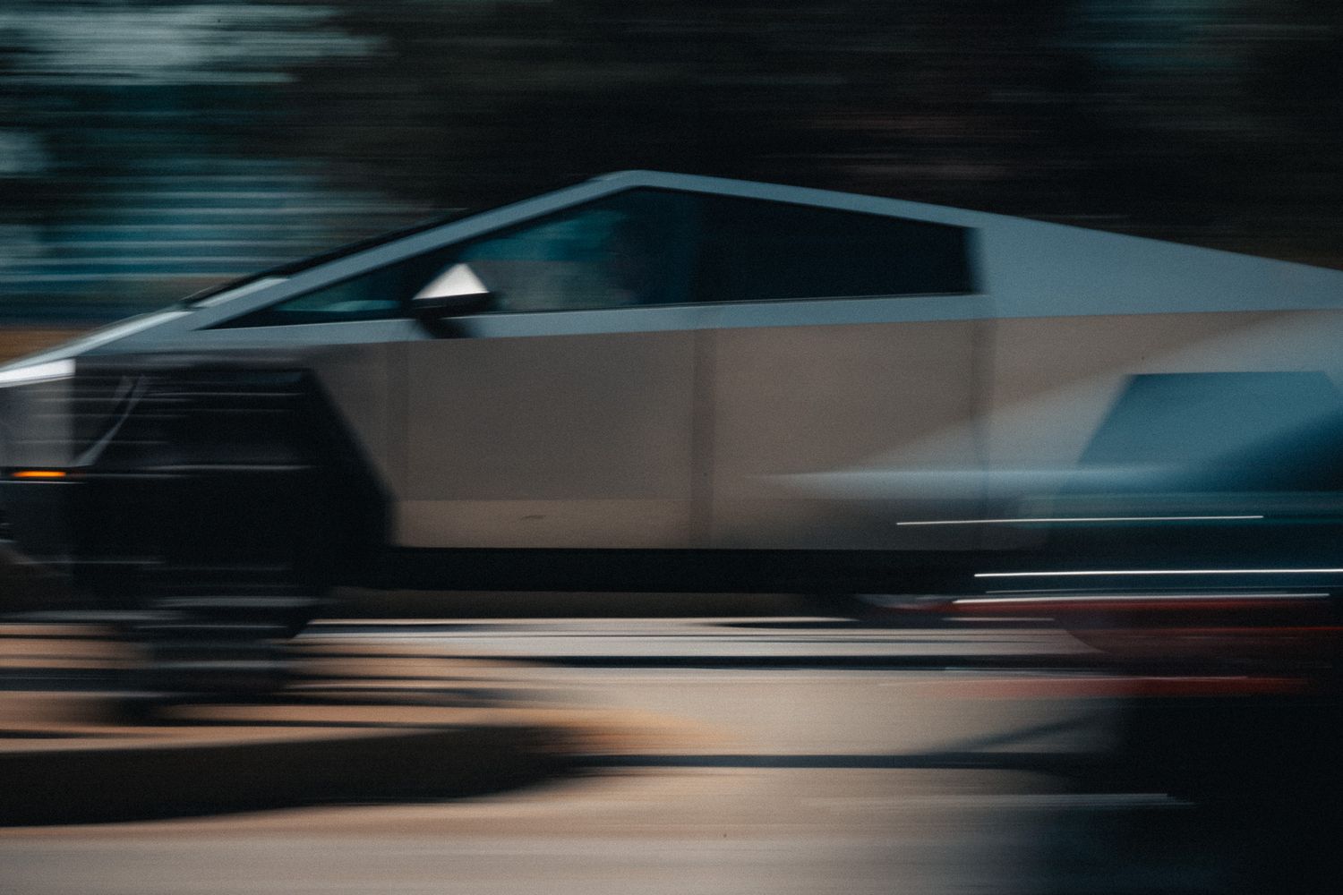 Tesla Cybertruck speeding on a road captured with motion blur effect showcasing its angular stainless steel design.