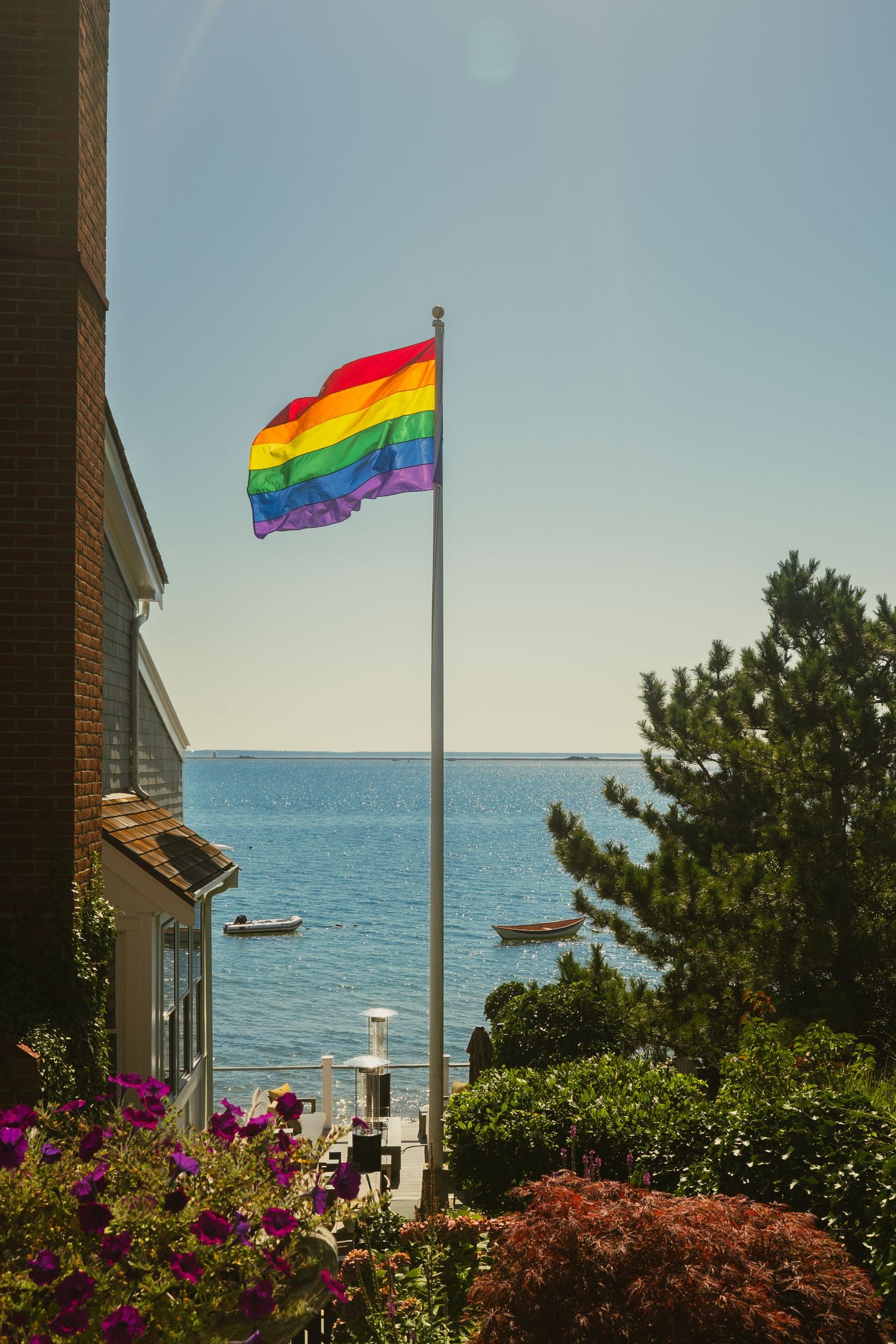 Rainbow Pride flag flying on a flagpole overlooking the ocean on a sunny day.