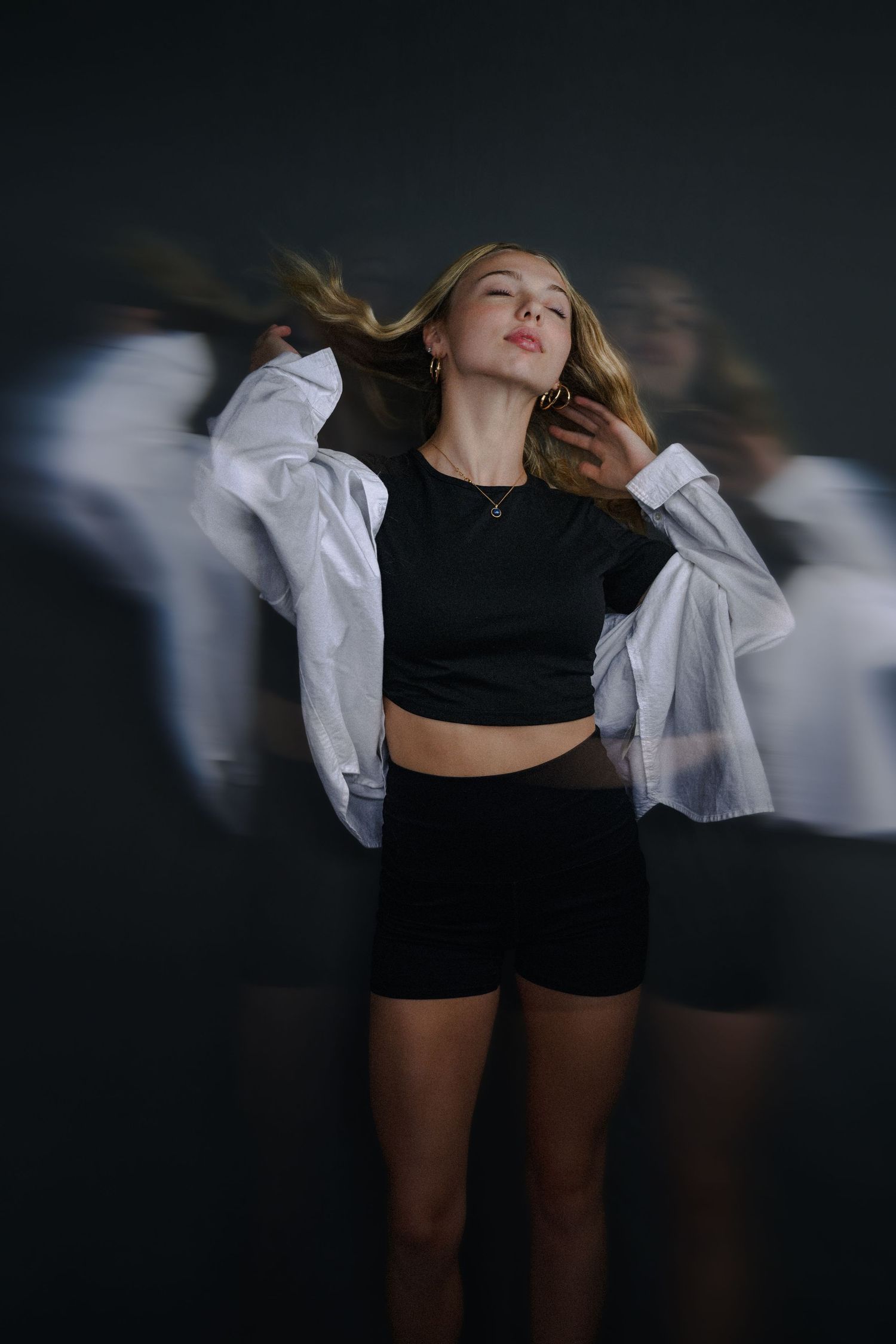 Blonde woman in black crop top and shorts poses dynamically with motion blur effect on dark background.
