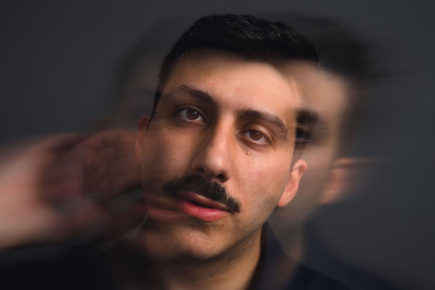 Young man with mustache in artistic multiple exposure portrait photography against dark background.