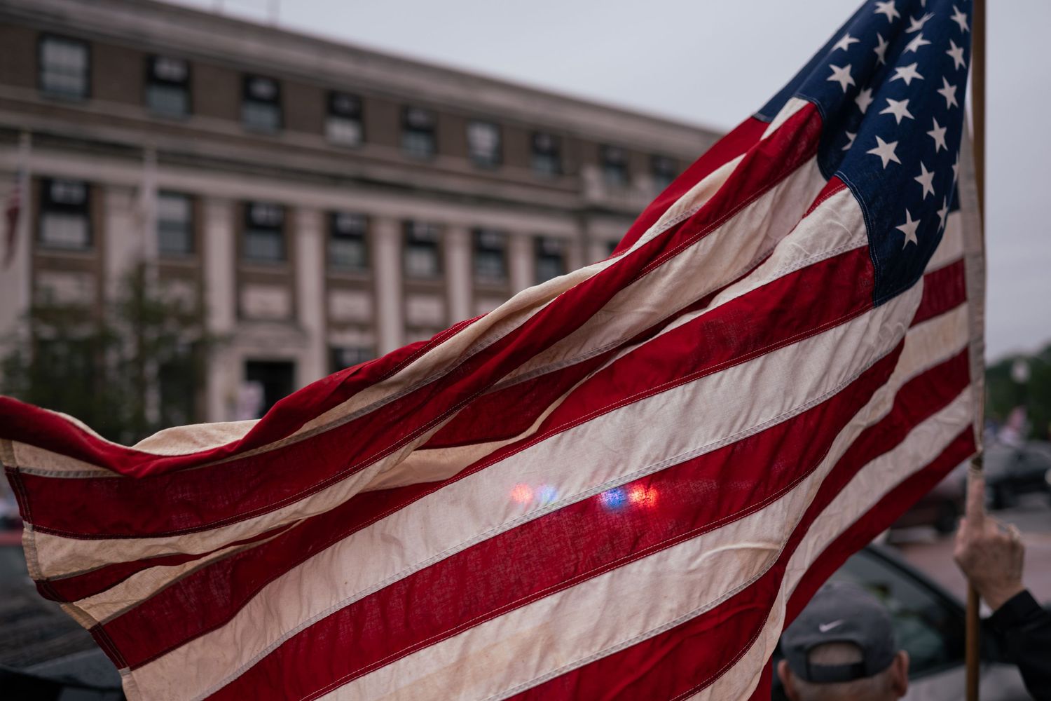 American flag waving in front of a government building during an outdoor rally or protest.