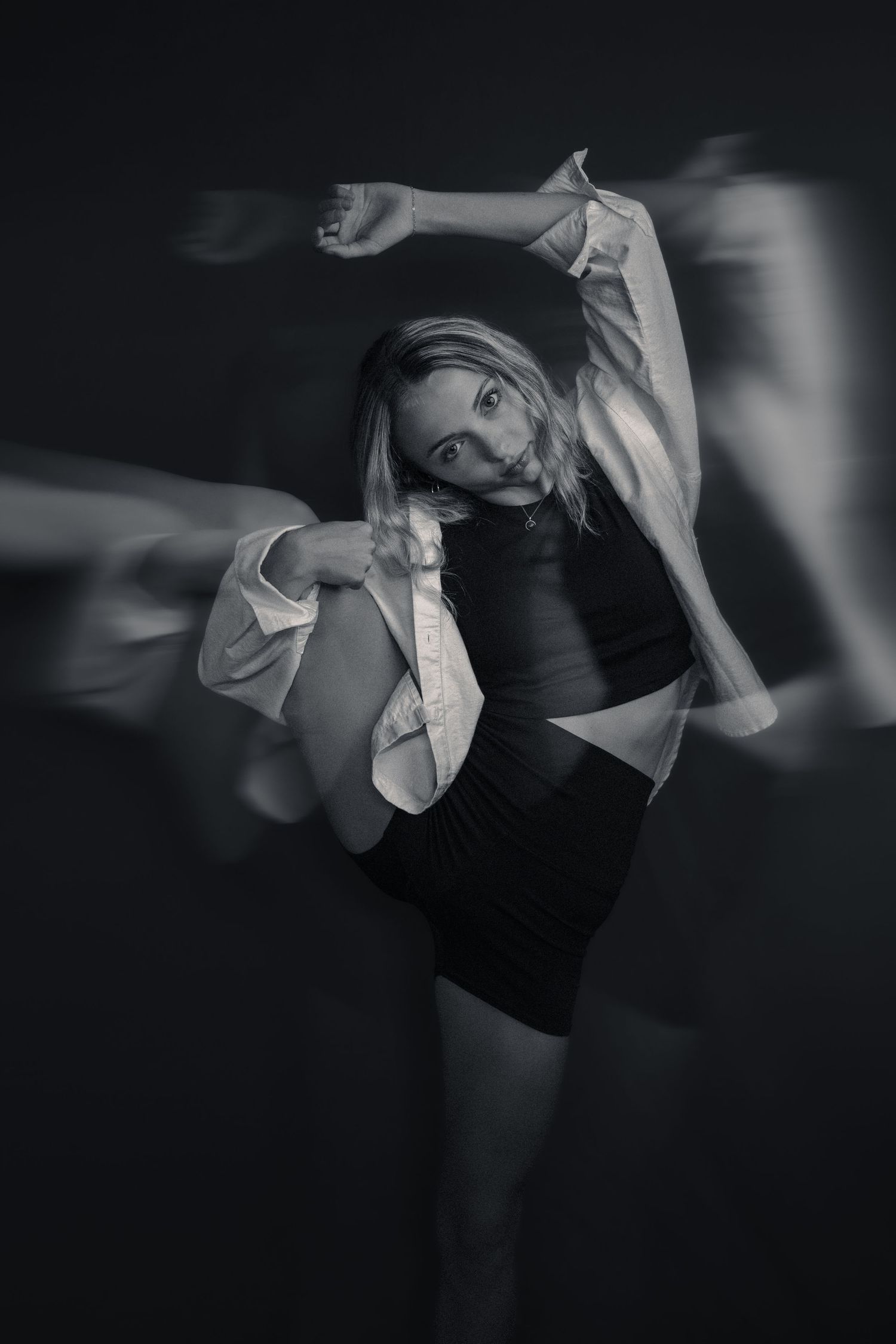 Black and white long exposure photo of a blonde woman dancing gracefully in a dark studio setting.