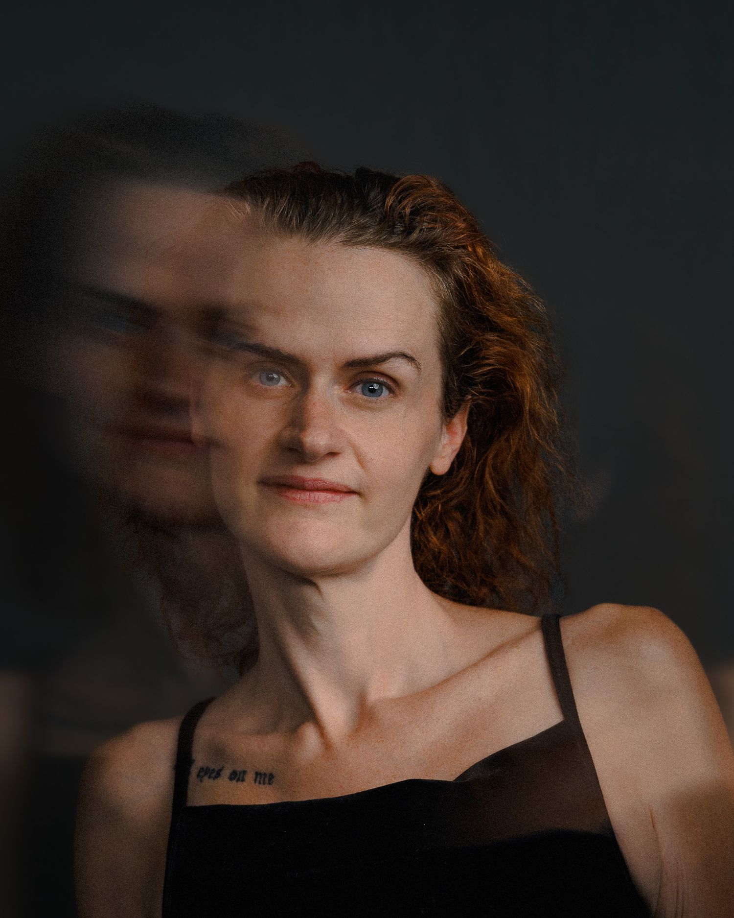 Woman with auburn hair and blue eyes poses with a motion blur double exposure effect against a dark background.