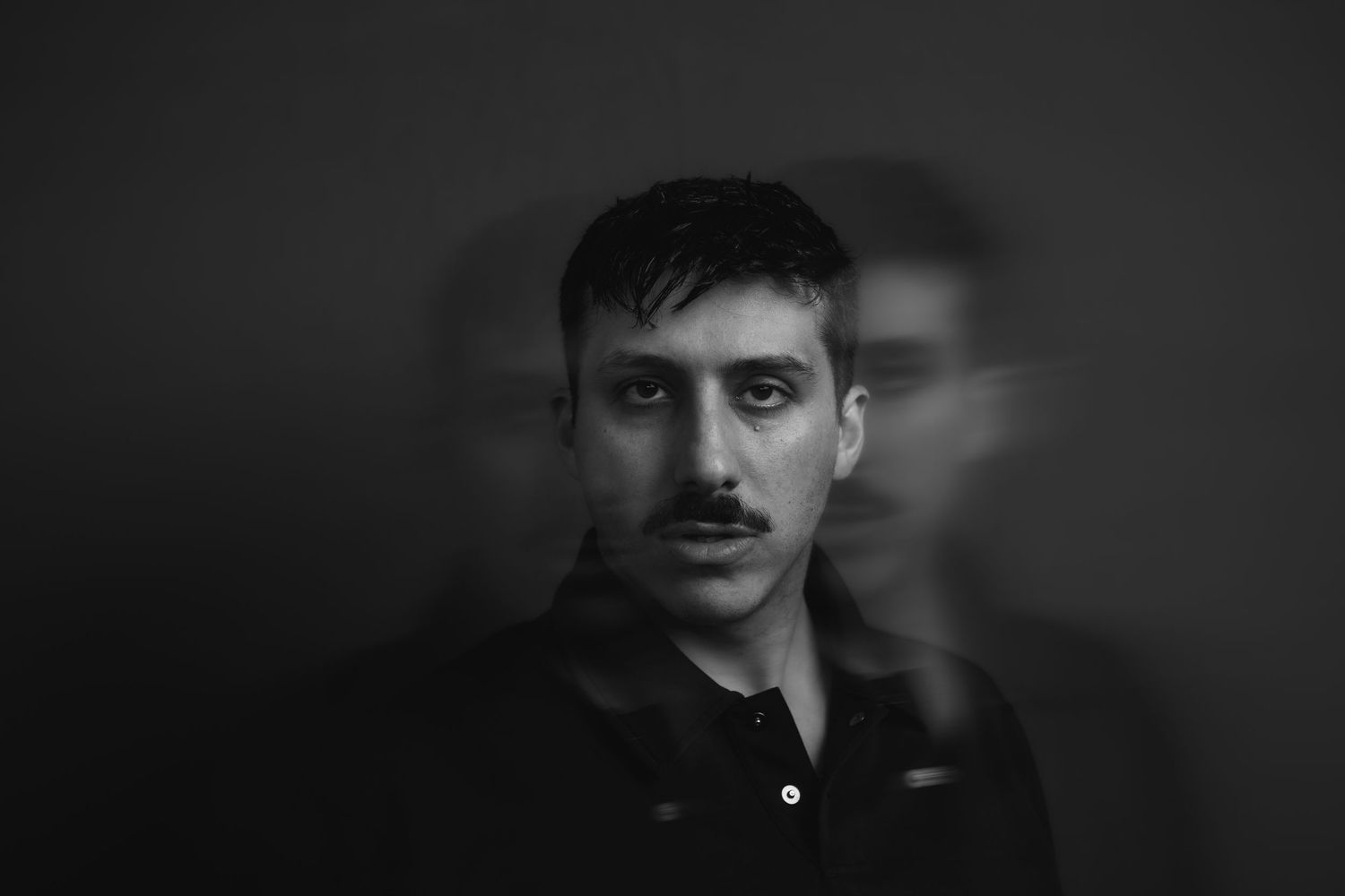 Black and white portrait of a young man with a mustache, artistic motion blur effect on dark background.