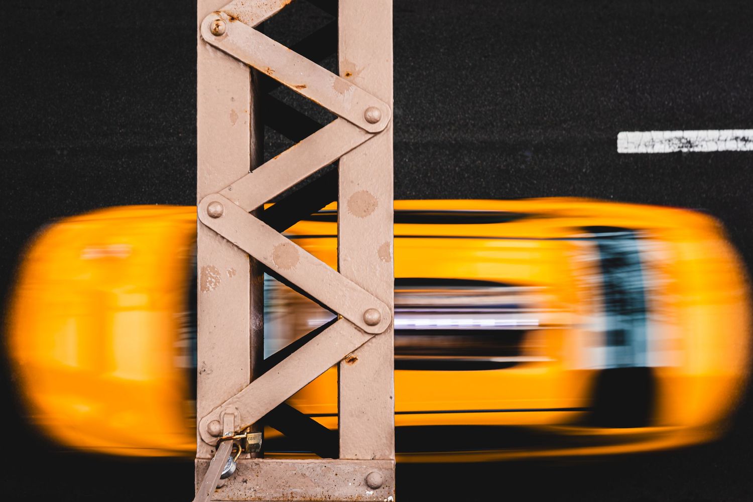 Aerial view of a yellow taxi cab speeding across a metal bridge, captured with motion blur.