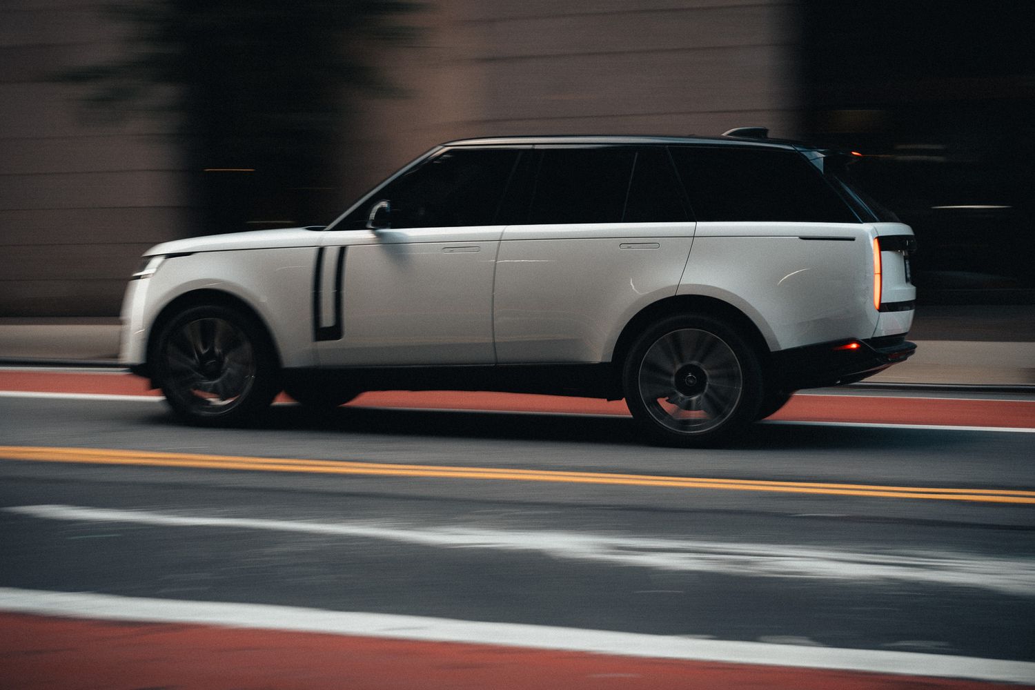 White Range Rover SUV speeding through city street, motion blur background, red curb, urban luxury vehicle in motion.