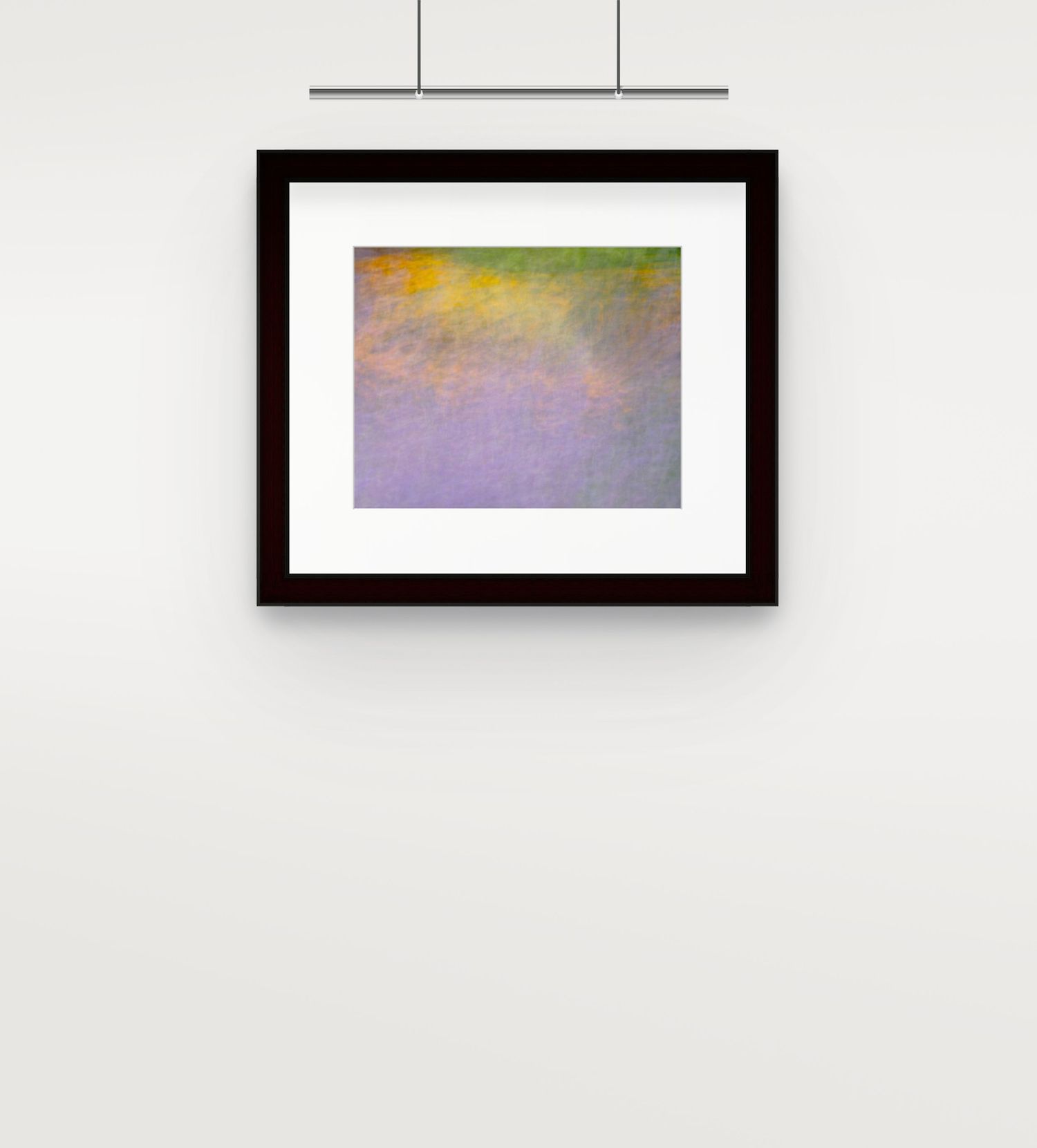 Framed abstract impressionist painting with soft purple, green and yellow hues on wall.