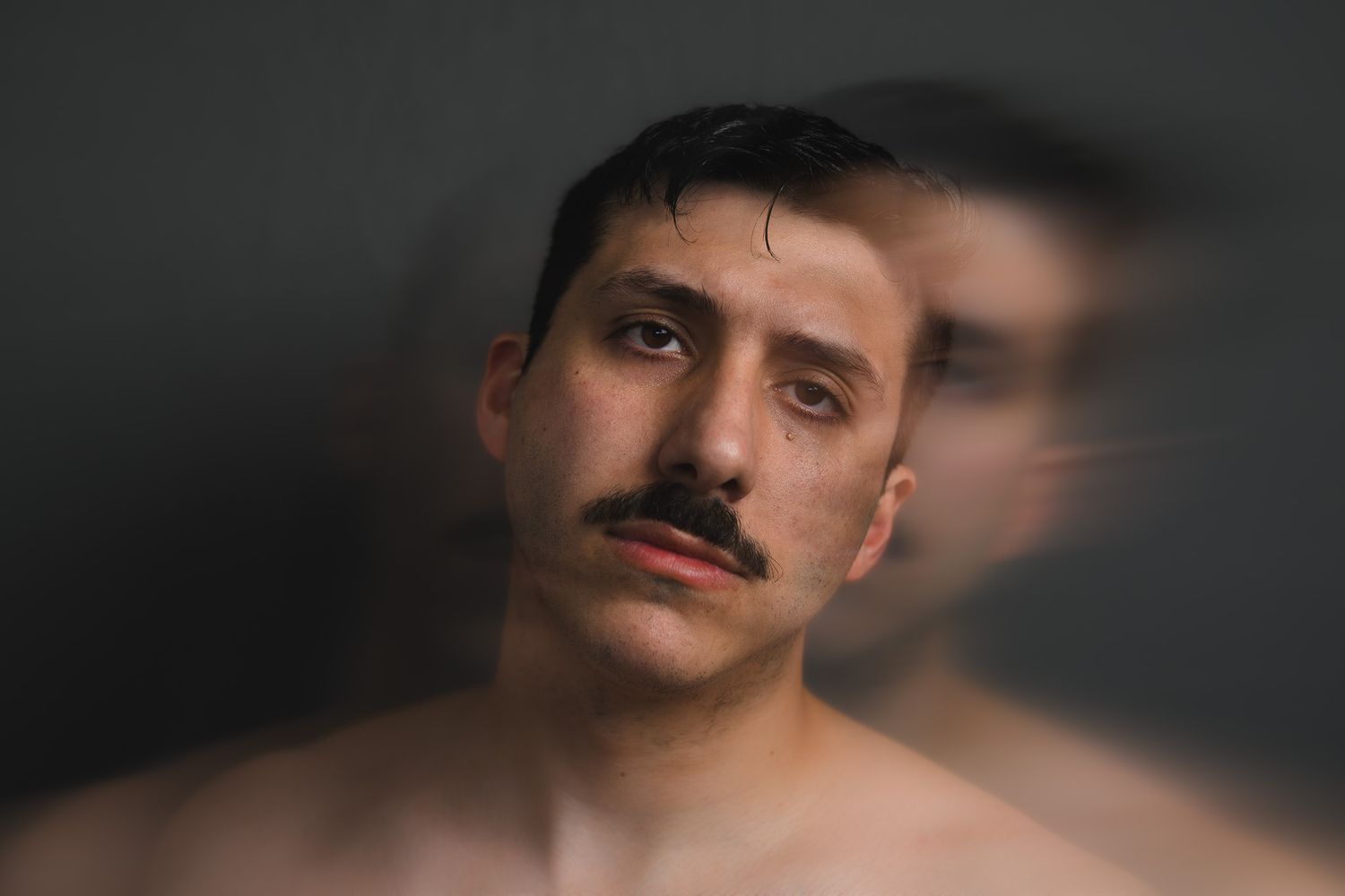 Shirtless man with mustache and tears, artistic double exposure portrait photography on dark background.