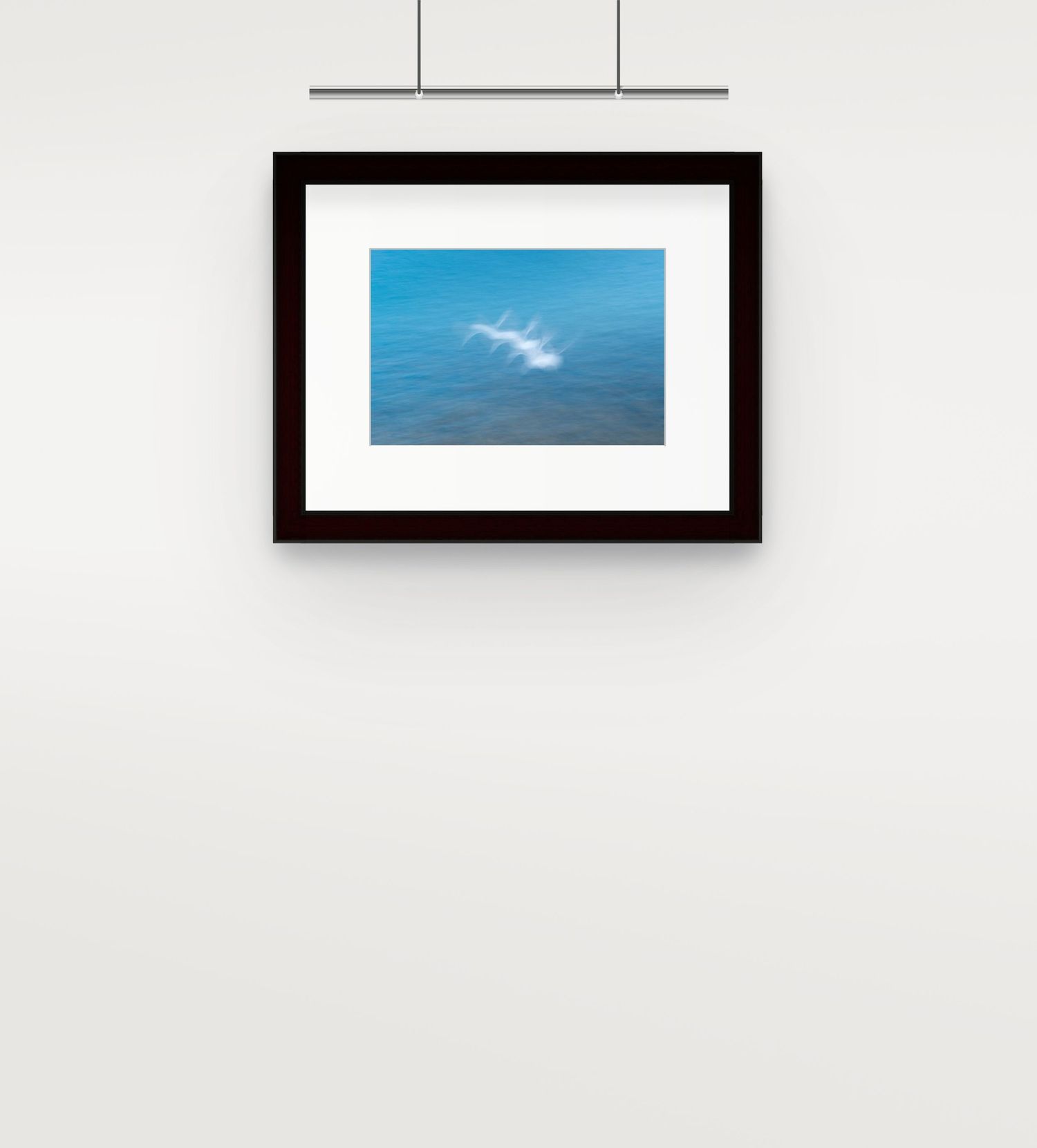 Framed abstract photo of seagulls in motion over blue ocean water hanging on wall.