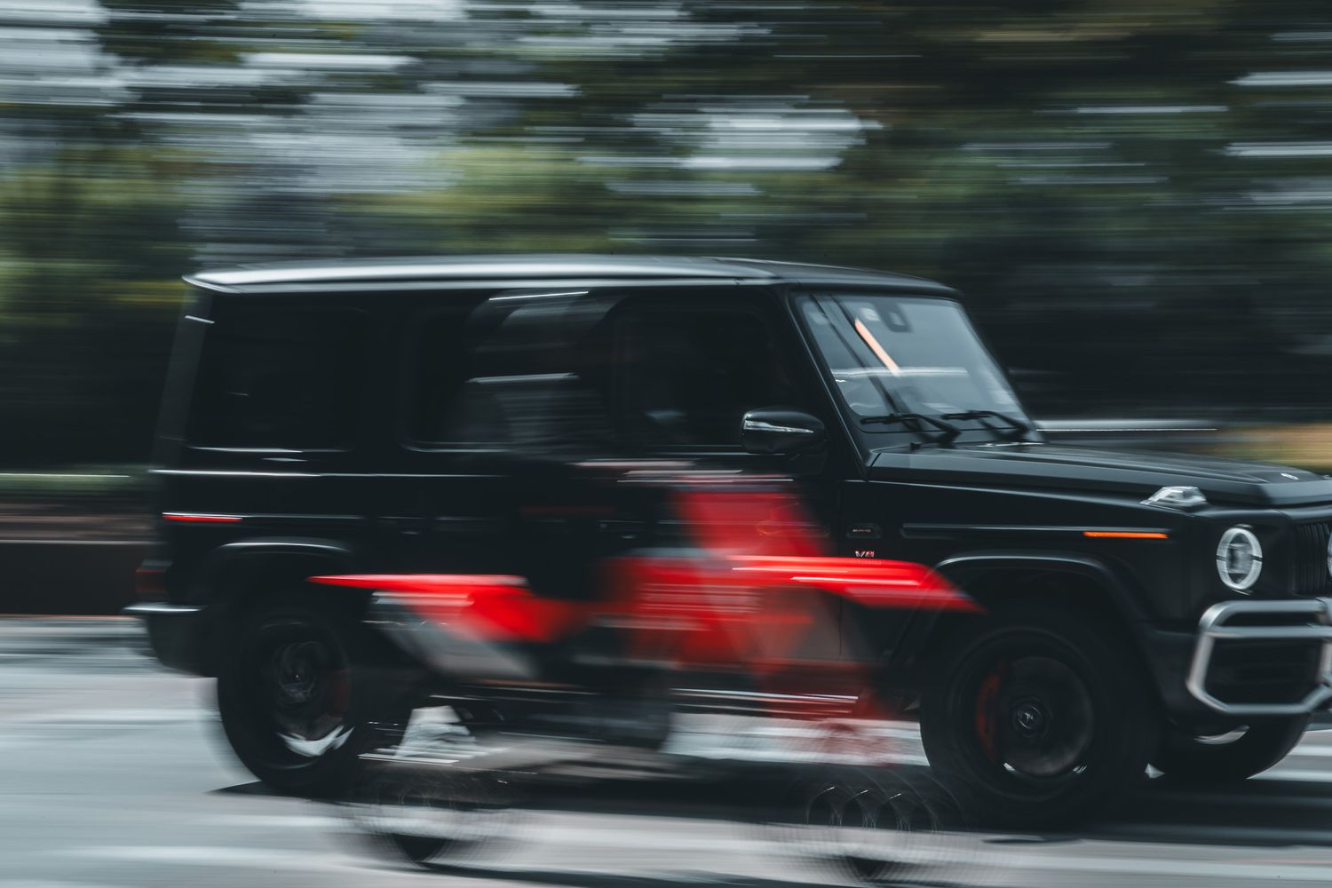 Black Mercedes-Benz G-Wagon SUV speeding on a road with motion blur effect and red accent details visible.