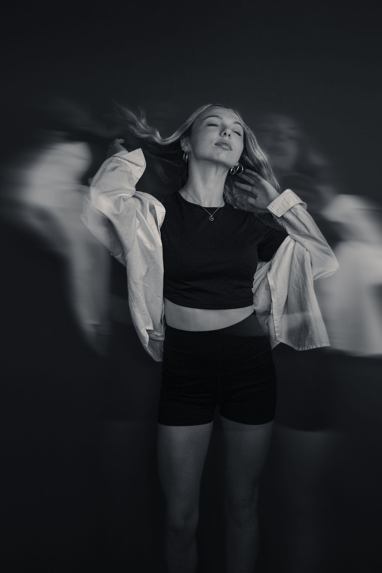 Black and white photo of a young woman dancing confidently in crop top and shorts with motion blur effect.