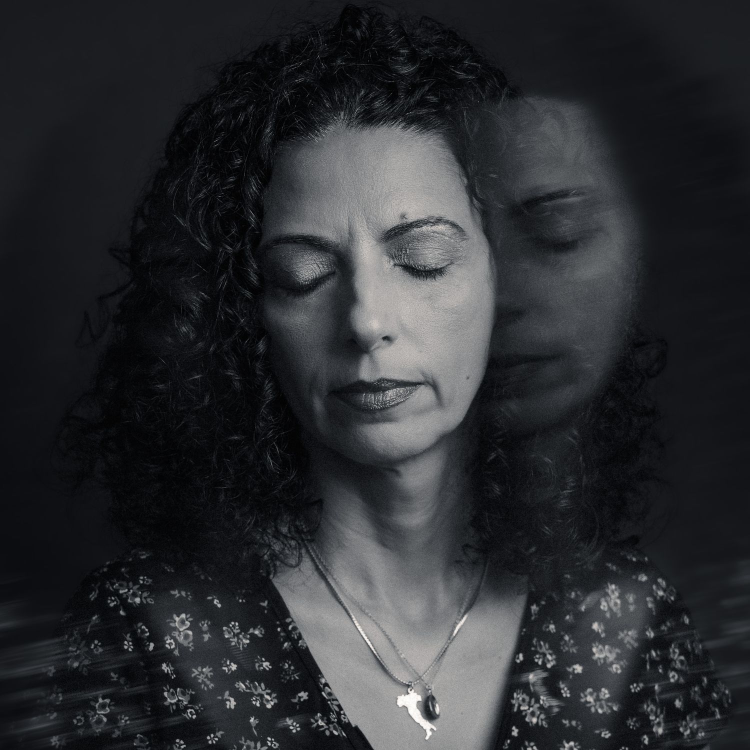 Black and white double exposure portrait of a woman with curly hair and closed eyes wearing a floral blouse.