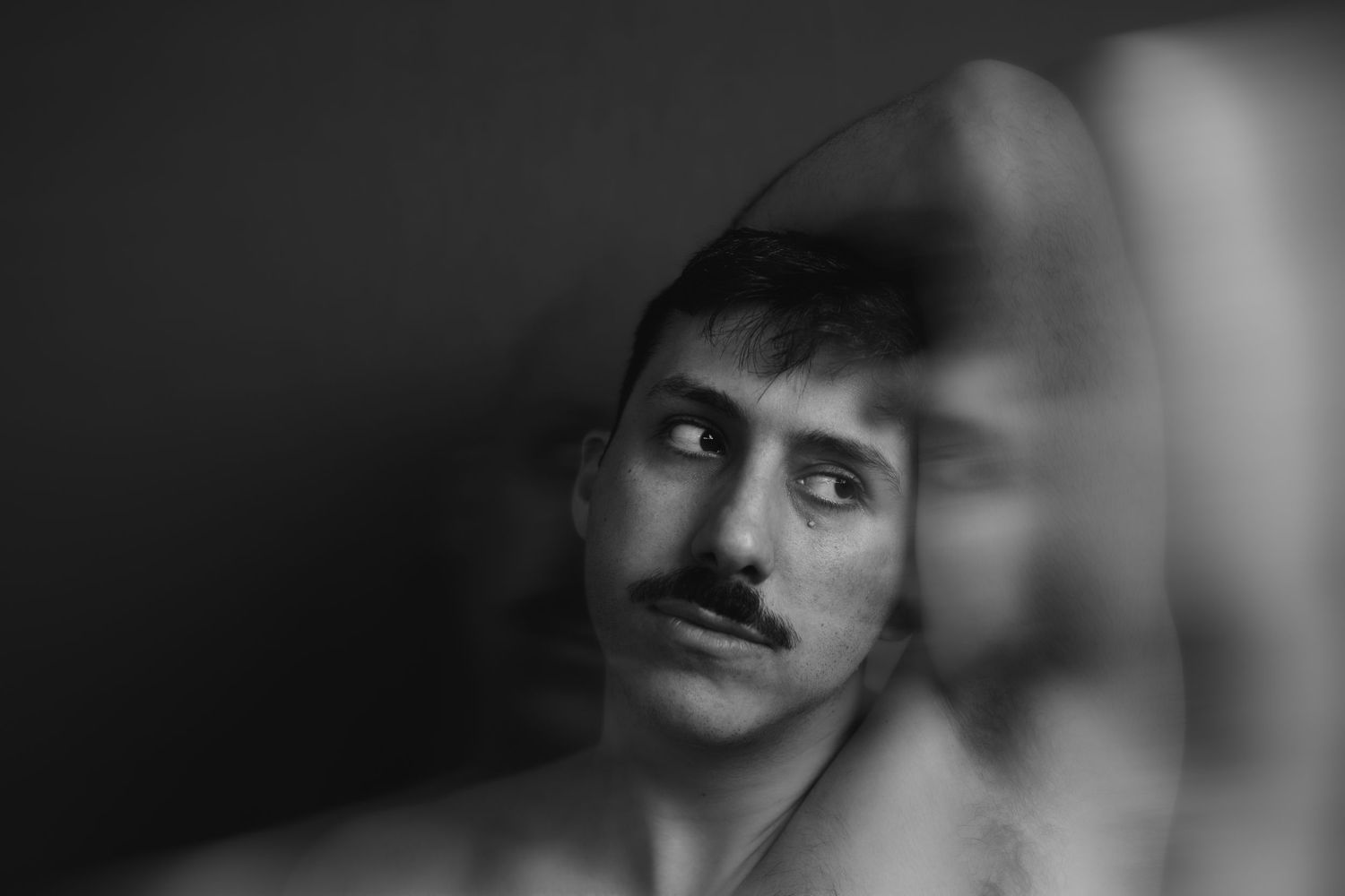 Black and white portrait of a young man with a mustache gazing upward, with artistic mirror reflection effect.
