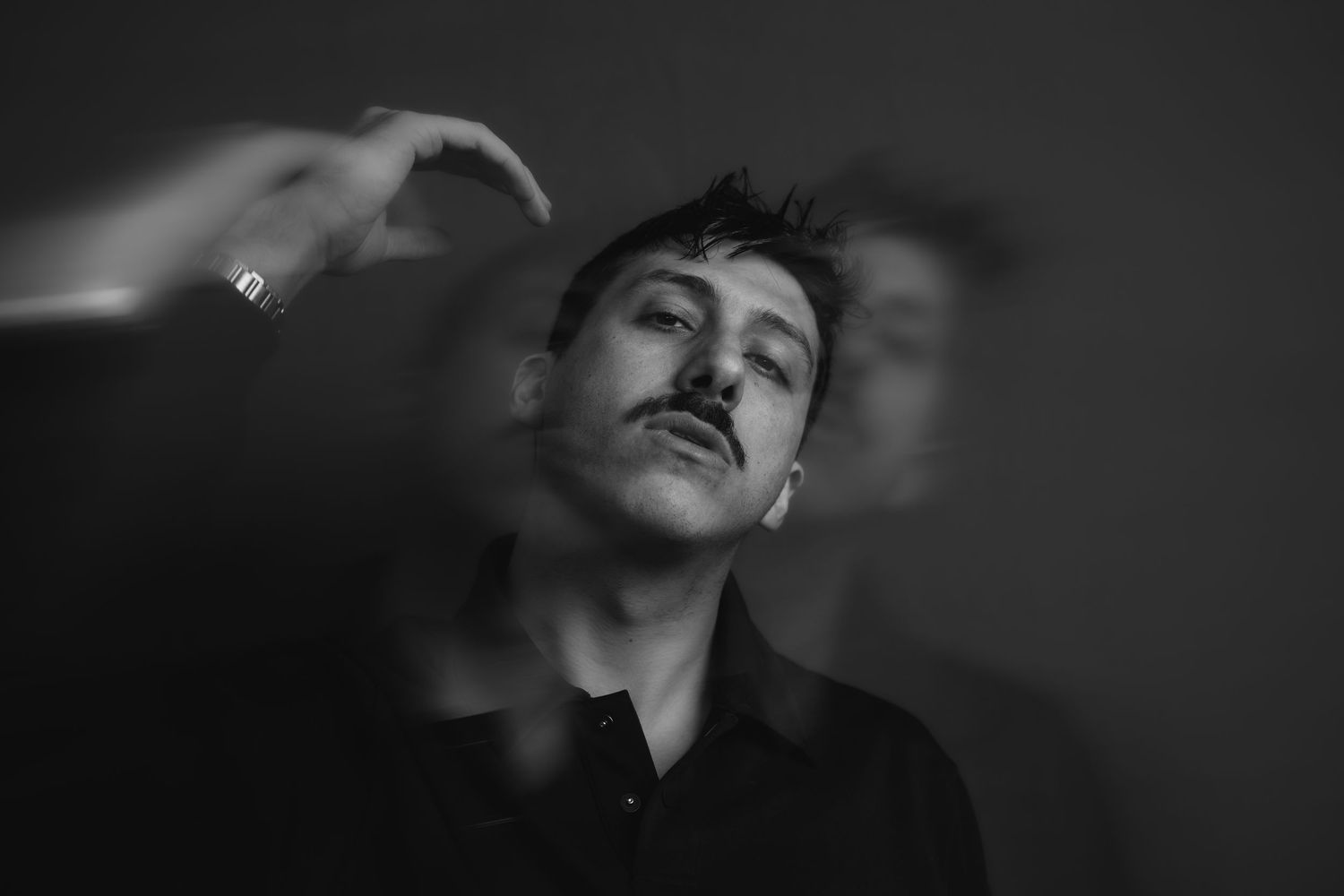 Black and white portrait of a young man with mustache, artistic motion blur effect, moody dramatic lighting.