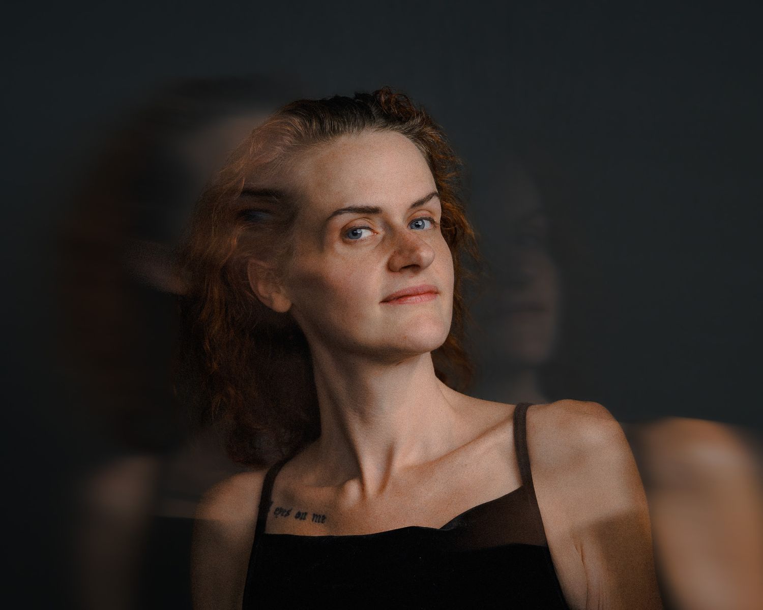 Young woman with short curly hair gazes upward against dark background with artistic motion blur effect.