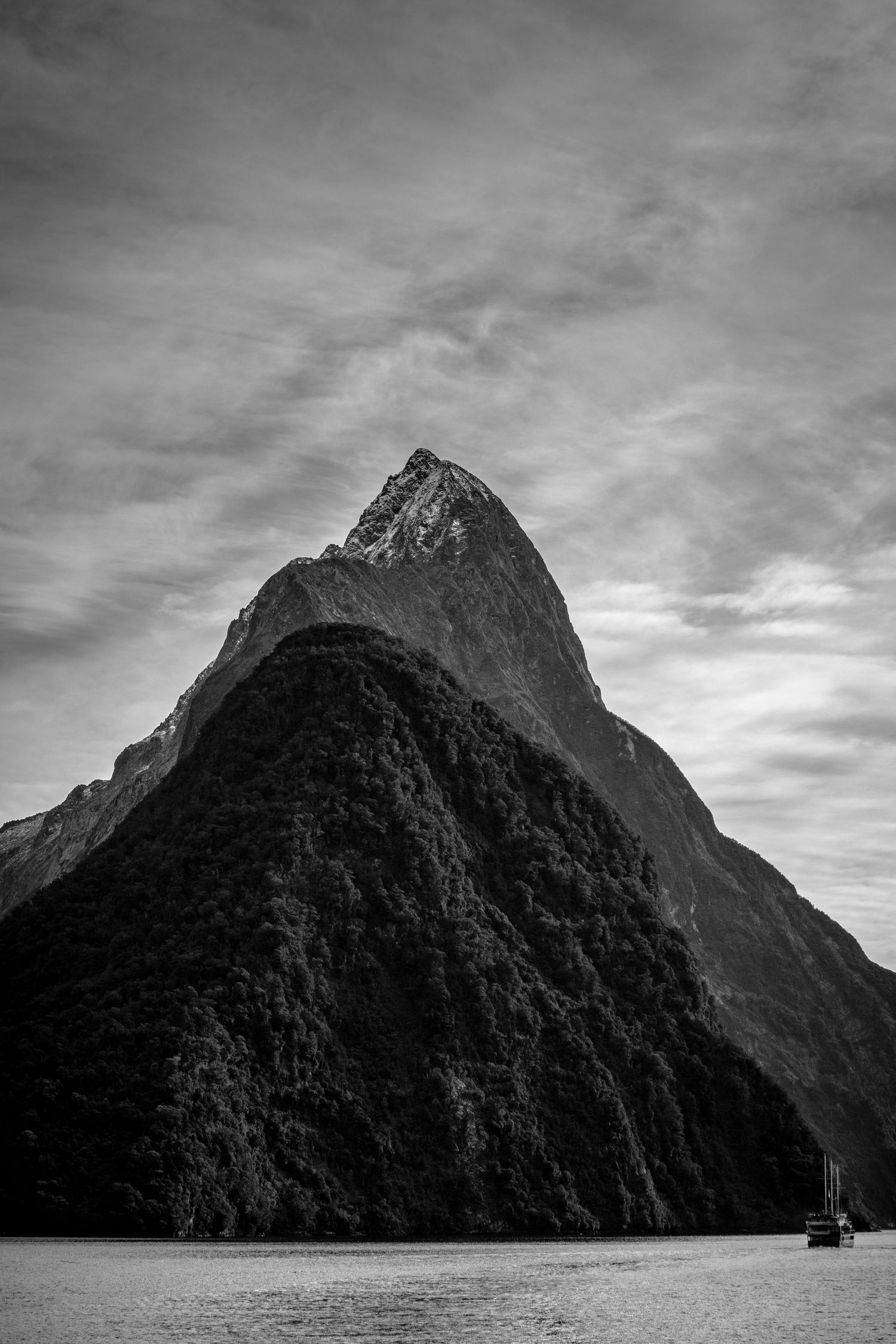 Mitre Peak rises steeply above Milford Sound beneath a dramatic cloudy sky in Fiordland, New Zealand.