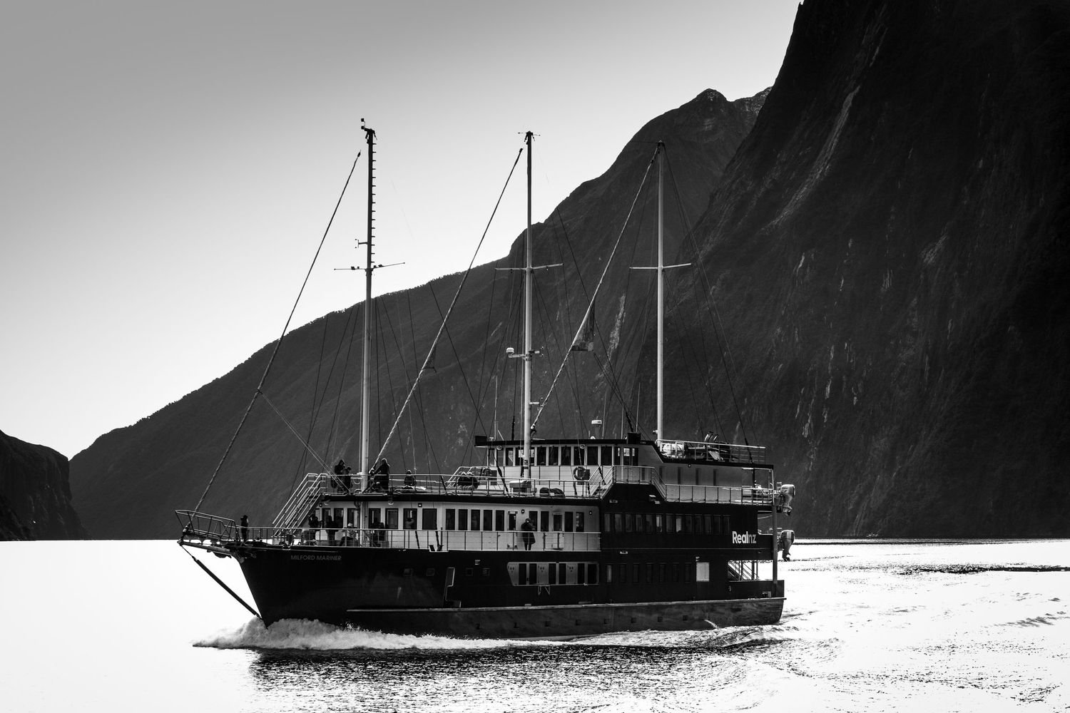 A cruise boat sails through Milford Sound, surrounded by towering mountains in Fiordland, New Zealand.