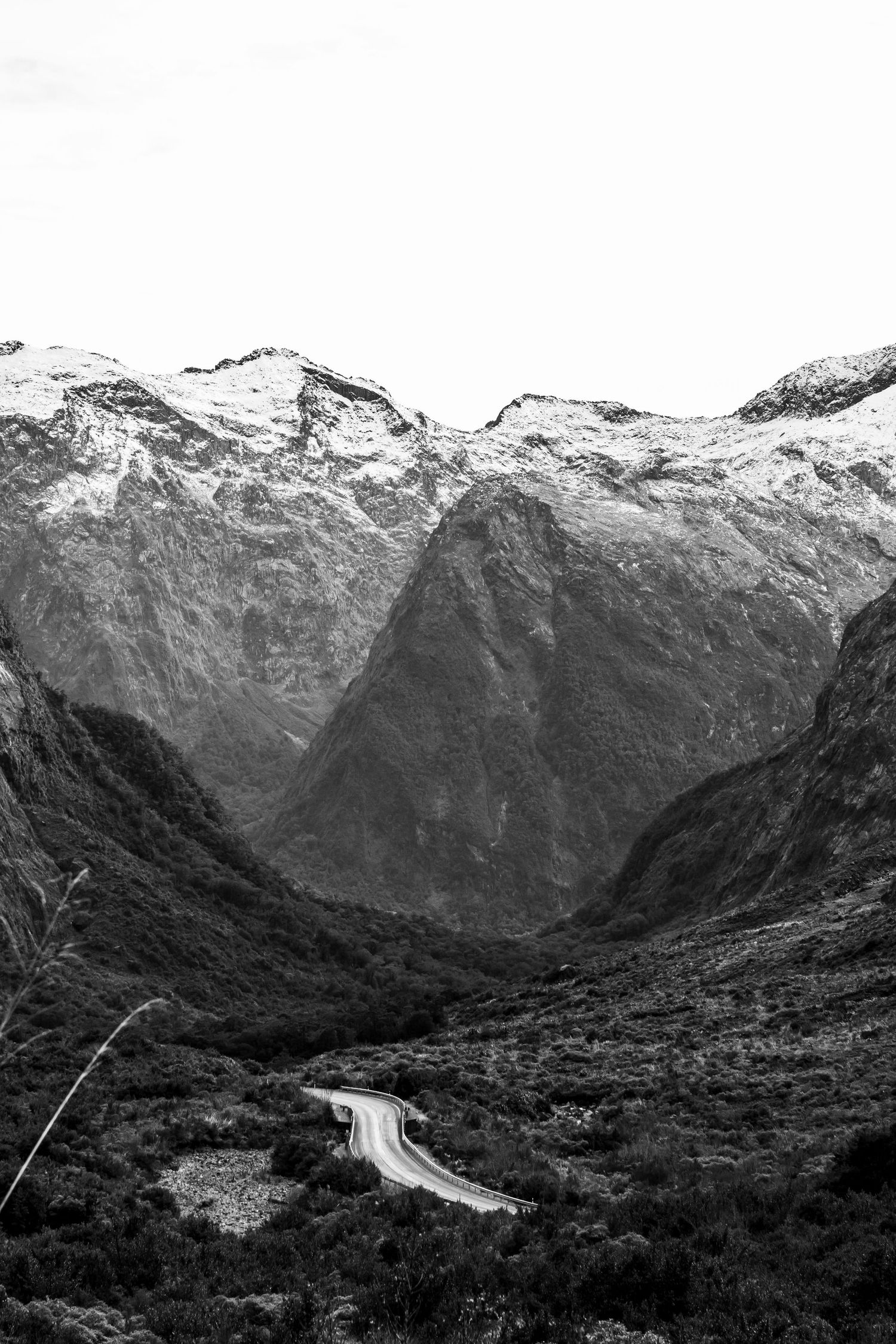 A winding road flows through a mountain valley beneath snow-capped peaks in Fiordland National Park, New Zealand.