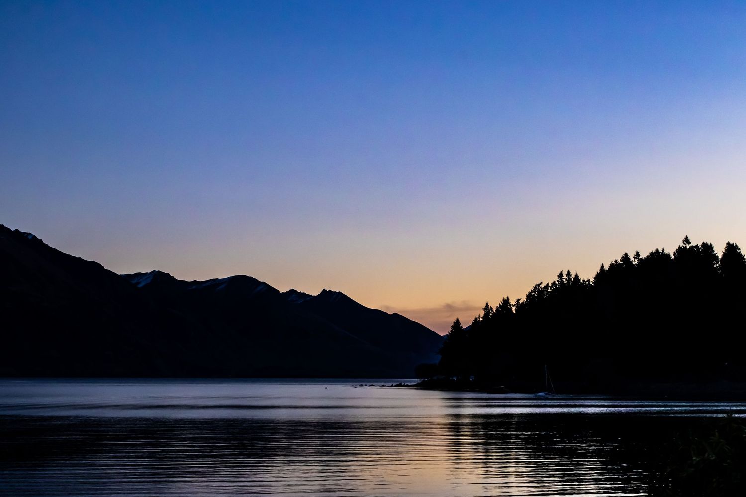 Mountain silhouettes surround the calm waters of Lake Wakatipu at sunset near Queenstown, New Zealand.