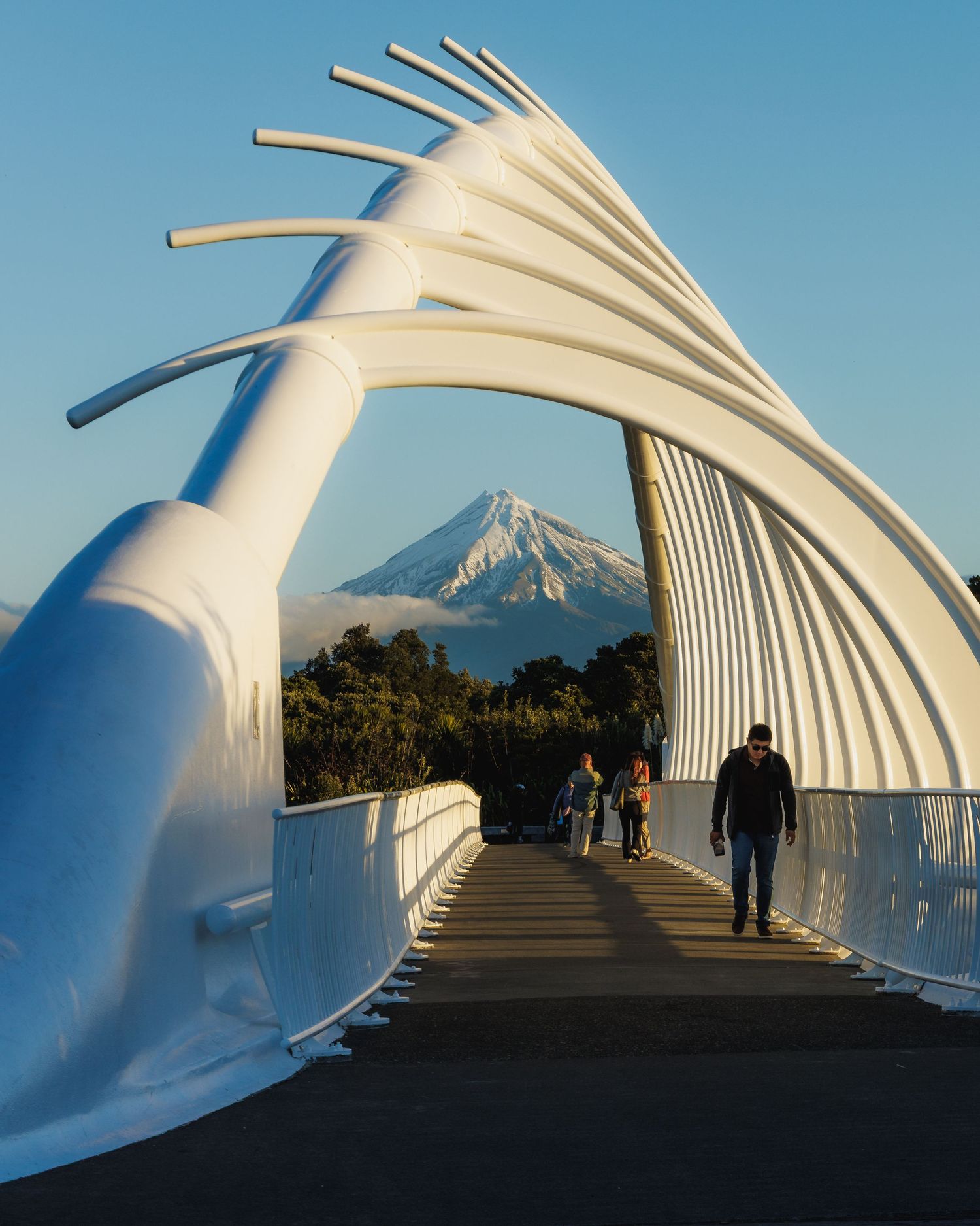 Te Rewa Rewa Bridge framing snow-covered Mount Taranaki in warm evening light, New Plymouth, New Zealand.