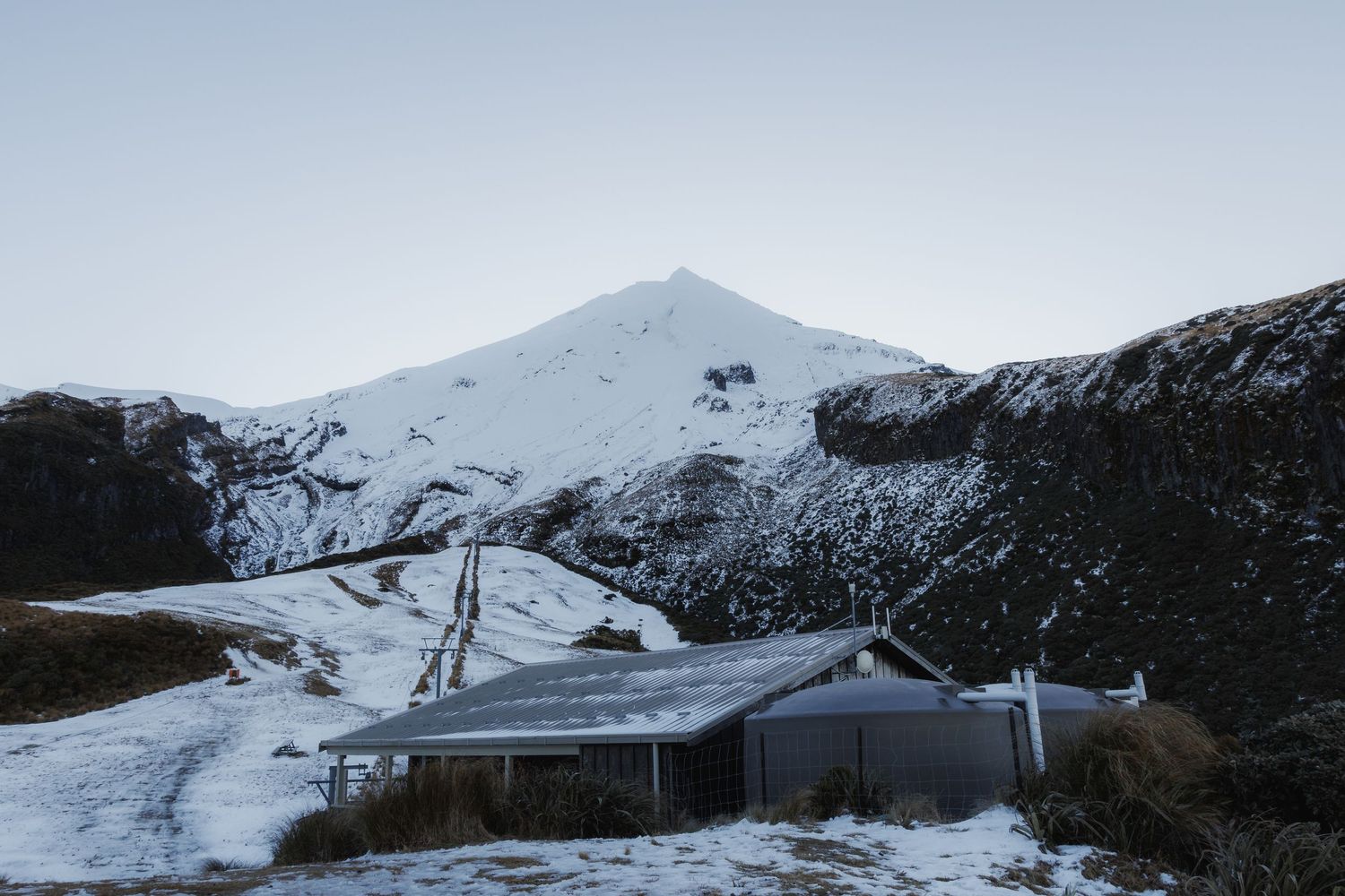 A ski-field building and lift line sit beneath the snow-covered slopes of Mount Taranaki at Stratford Plateau.