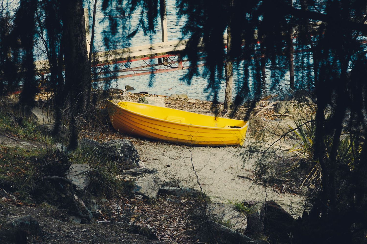 Bright yellow boat resting on the shore beside the water, partially framed by dark trees.