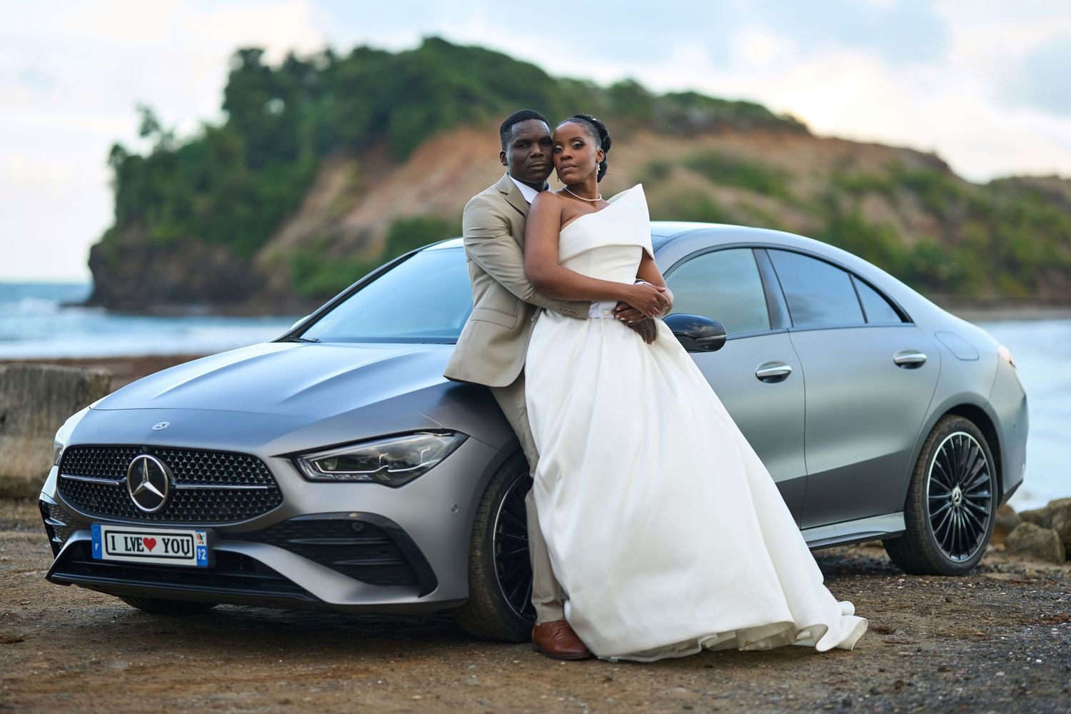 Des mariés enlacés contre leur mercedes avec le Tombolo de Sainte-Marie en fond Martinique