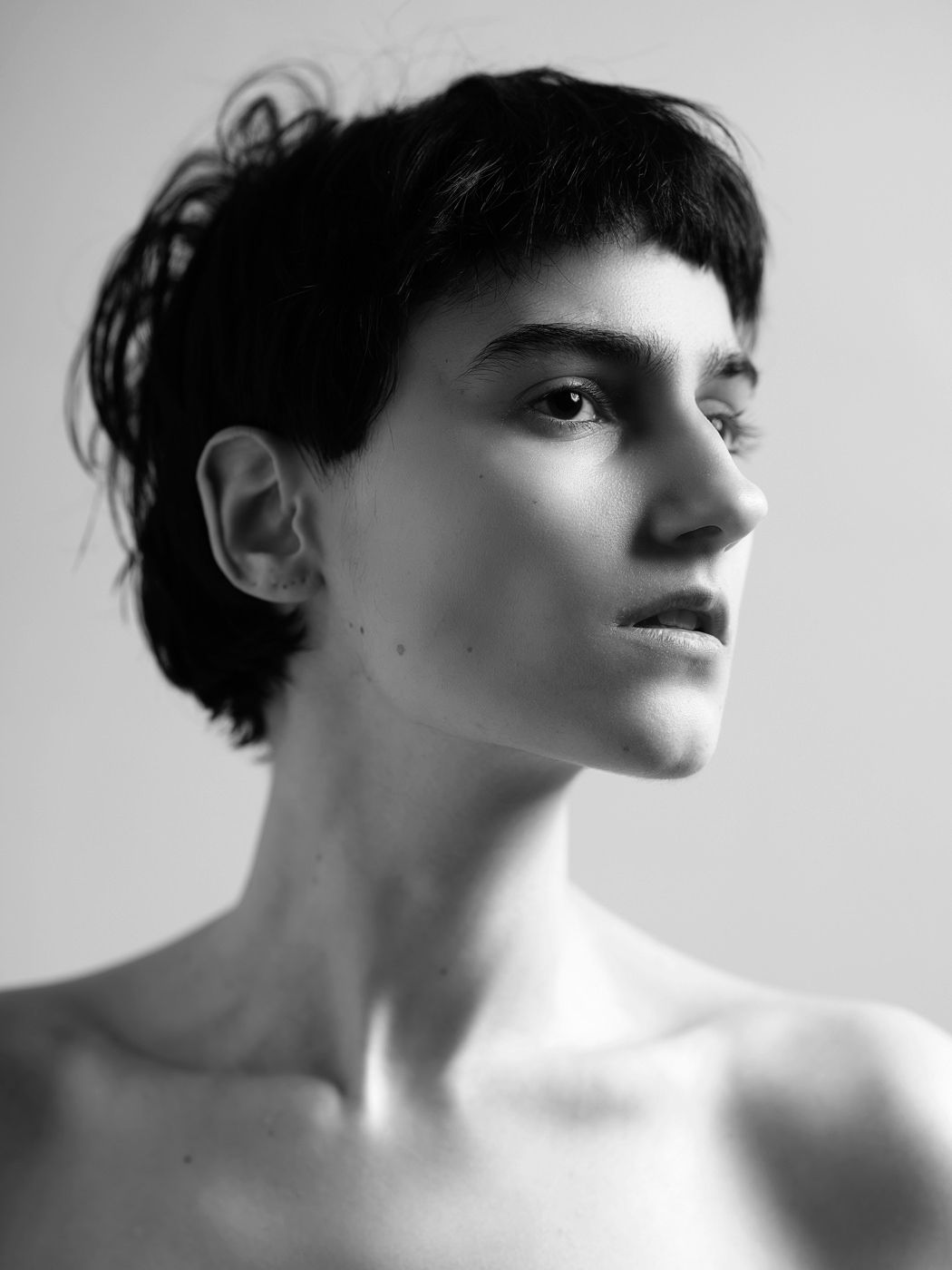 Black and white portrait of a young woman with short dark hair, gazing upward with bare shoulders.