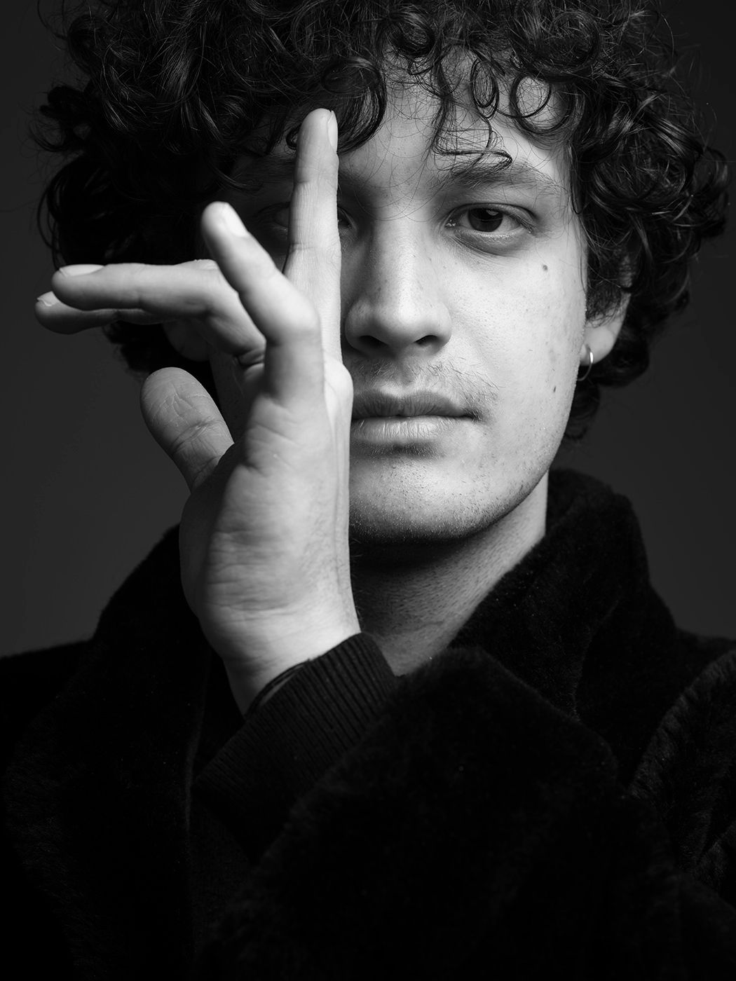 Black and white portrait of a young man with curly hair holding his hand up near his face. Balázs Elemér Jr.