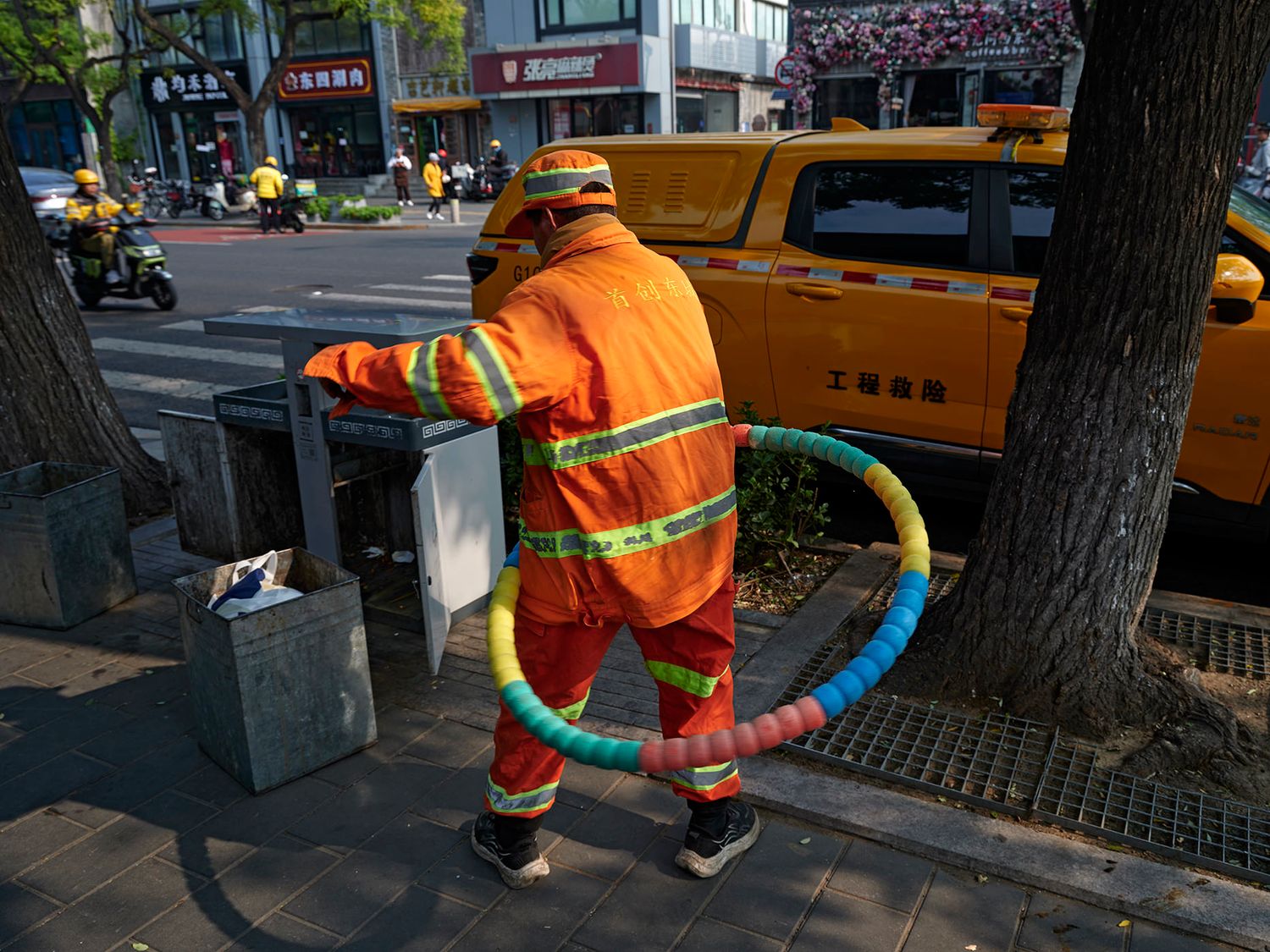 Orange uniformed street cleaner worker holding colorful hose on urban sidewalk in China.