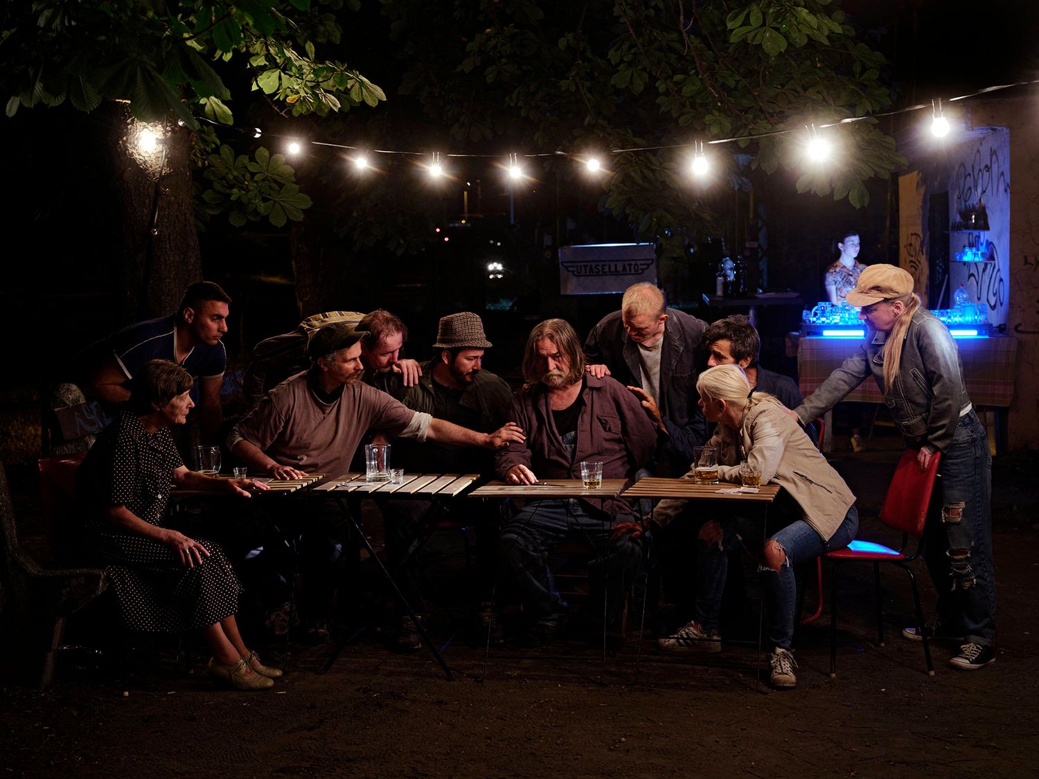 Group of people gathered around a long table outdoors under string lights at night.