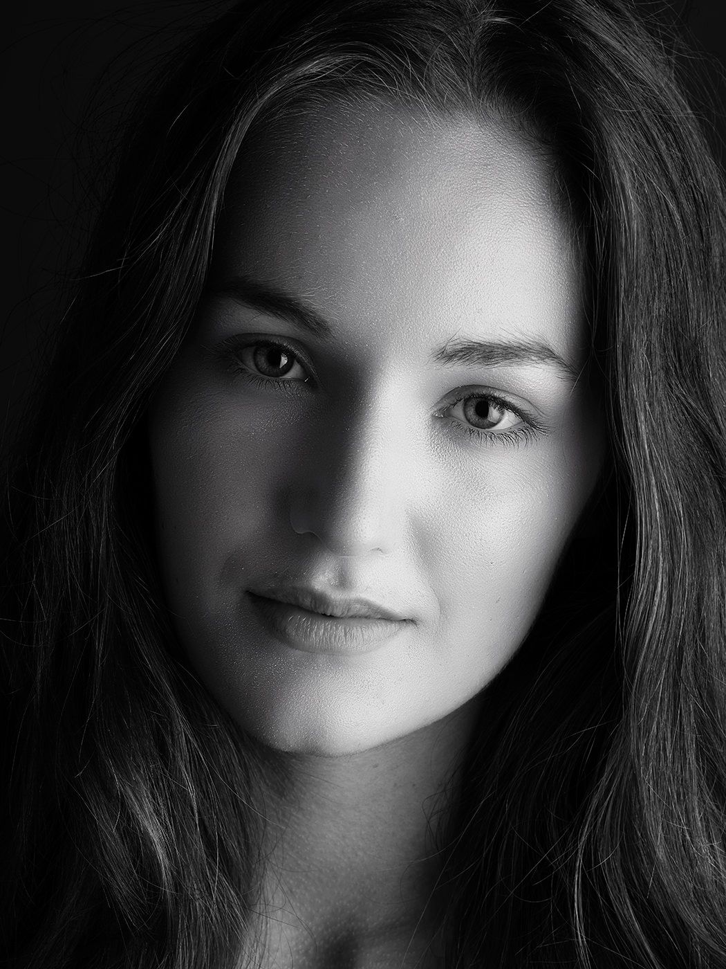 Black and white portrait of a young woman with long hair and a subtle smile against a dark background.