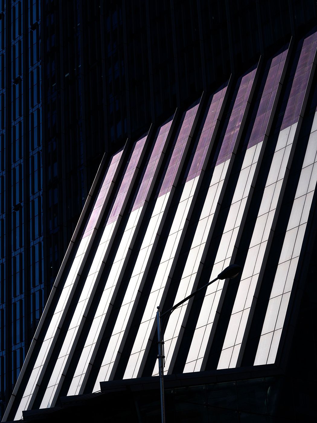 Abstract architectural detail of a modern building facade with vertical fins casting dramatic shadows in purple and white tones.
