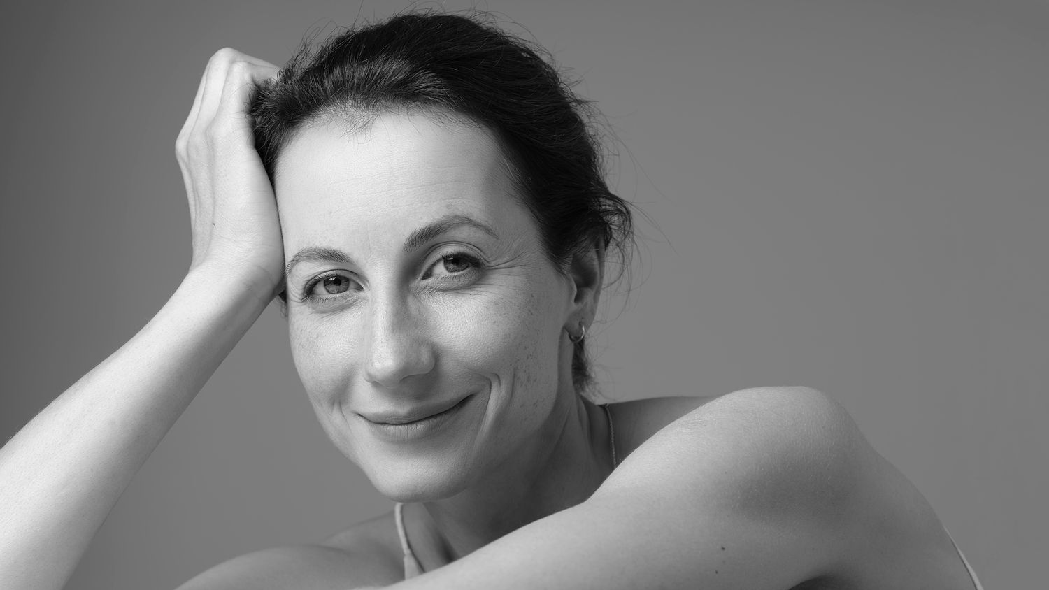 Elegant black and white close-up portrait of a smiling brunette woman resting chin on hands.