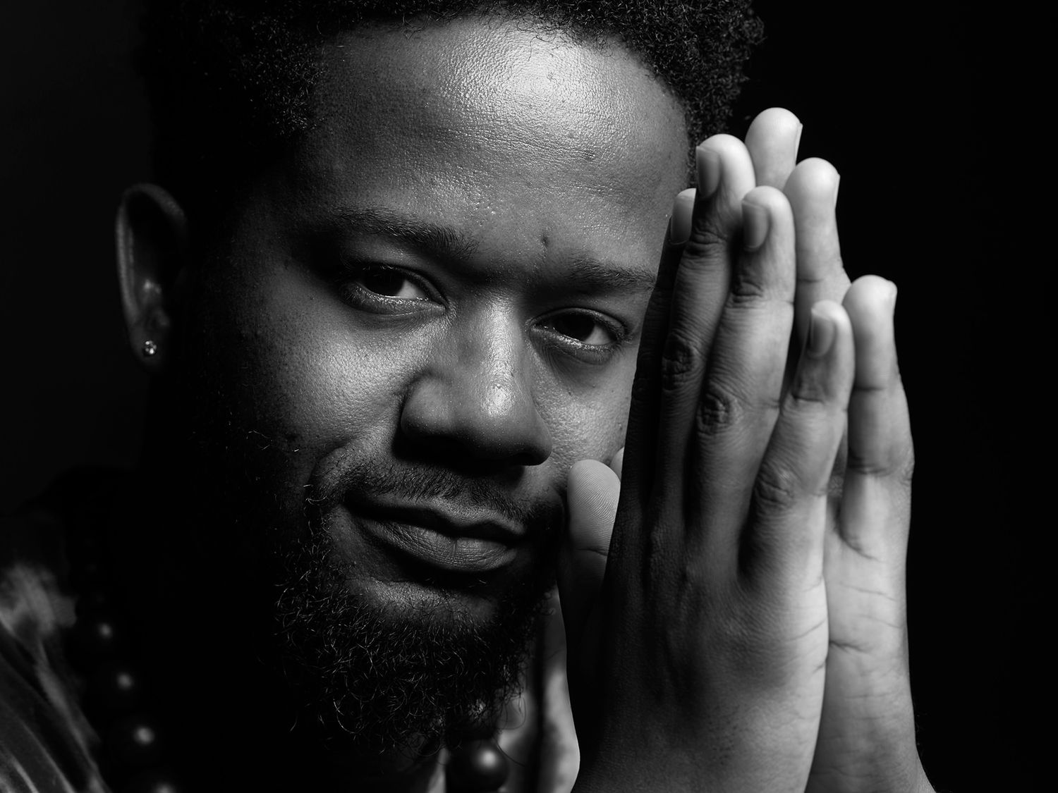 Black and white portrait of a bearded man with hands pressed together near his face, looking thoughtfully at camera. Ben Williams