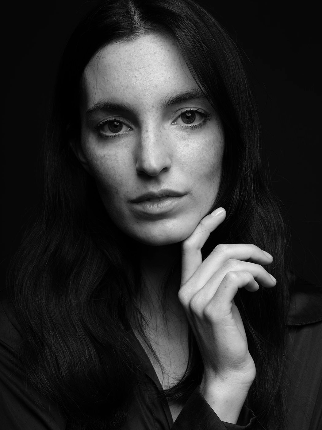 Black and white portrait of a young woman with long dark hair, freckles, resting chin on hand.