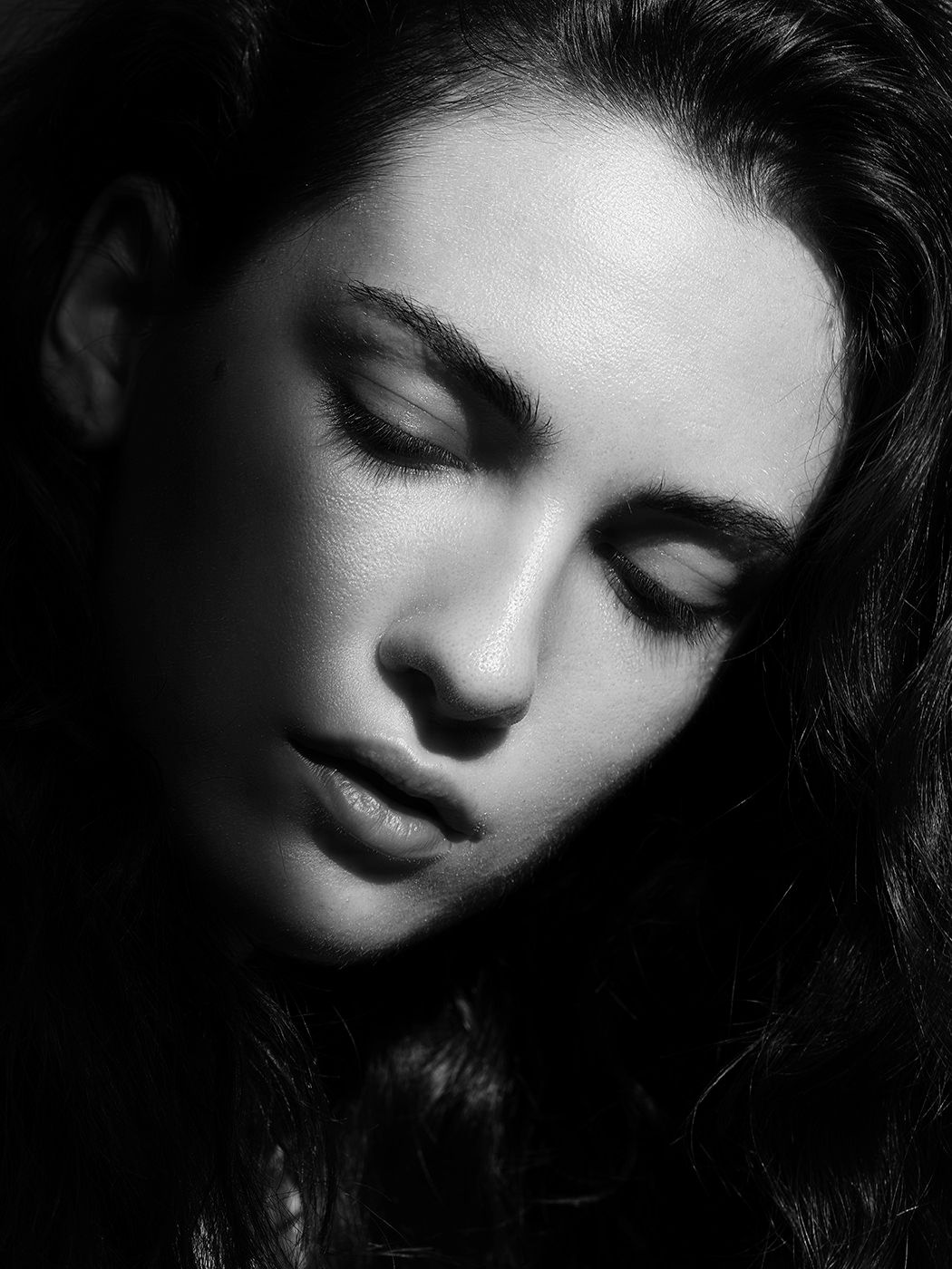 Black and white portrait of a young woman with closed eyes and dark wavy hair in dramatic lighting.