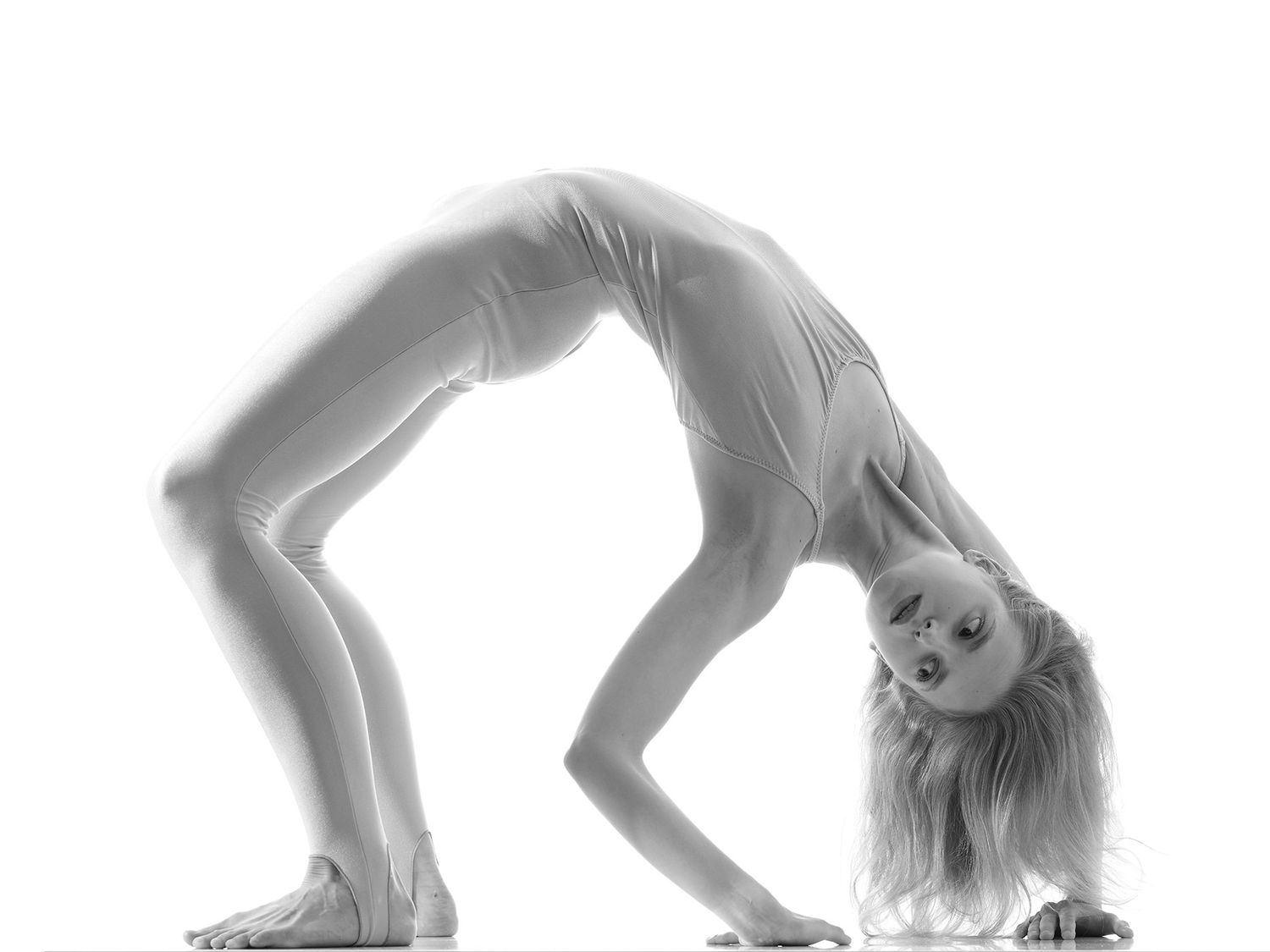 Black and white photo of a flexible woman performing a backbend bridge pose against a white background.