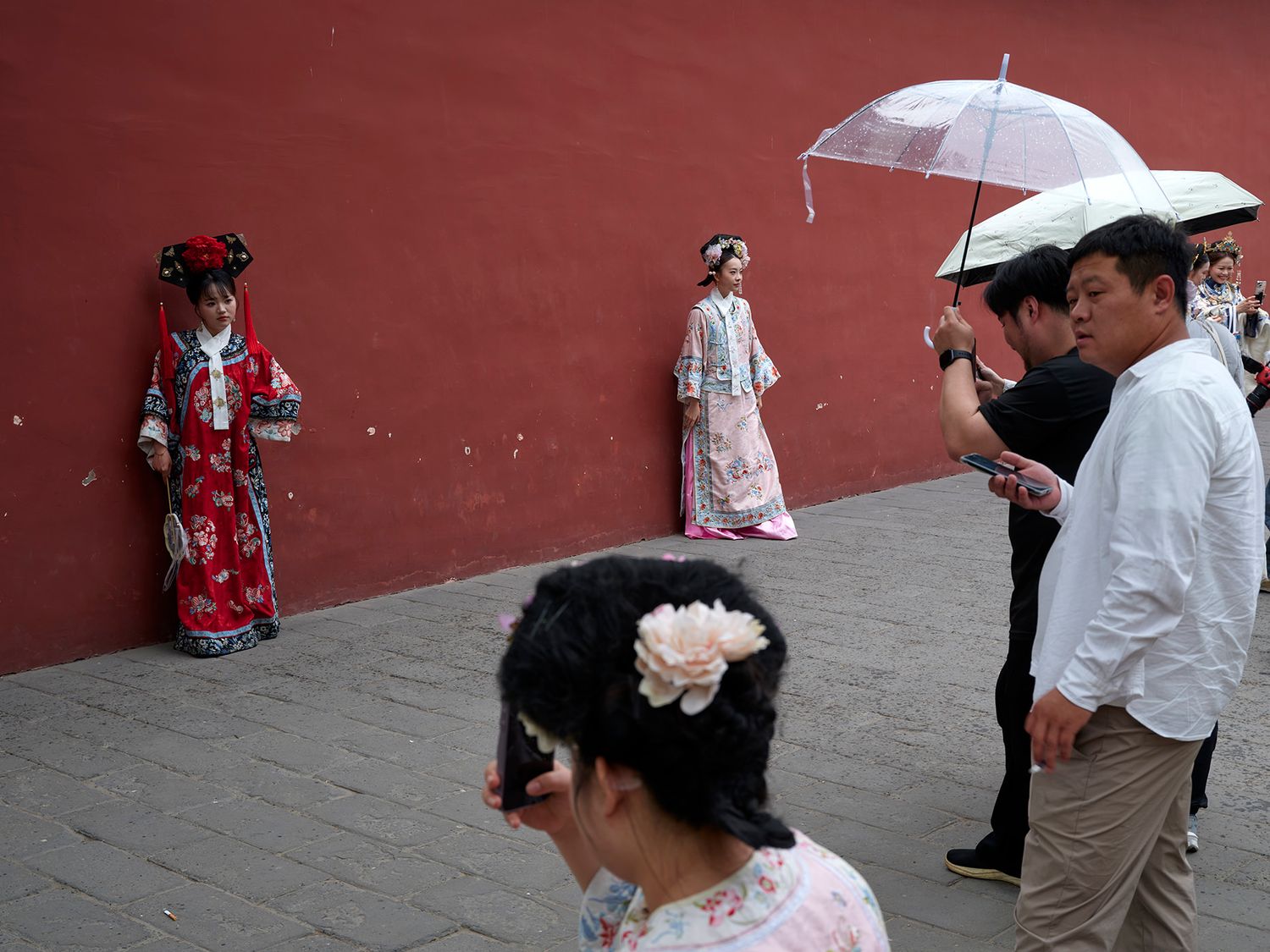 Tourists in traditional Chinese Hanfu costumes pose near a red wall, as visitors photograph them in Beijing.