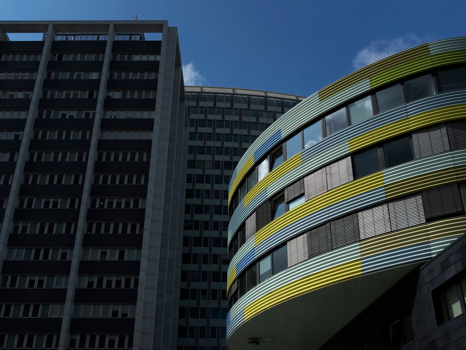 Two contrasting buildings: a dark rectangular tower and a modern curved structure with yellow and green striped facade.