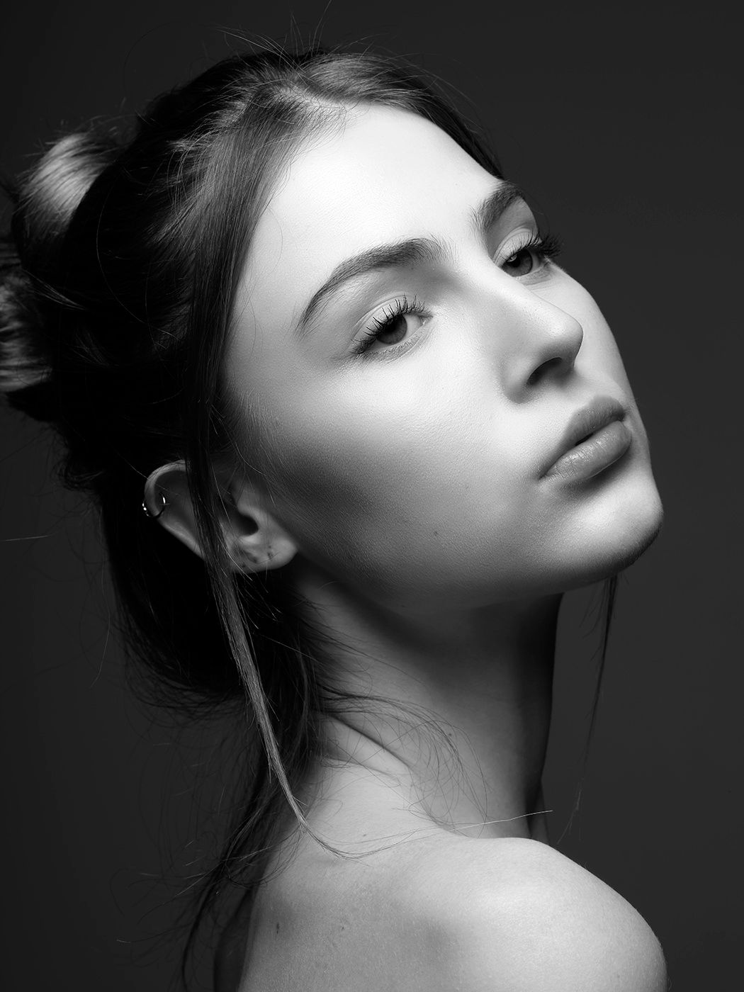Black and white portrait of a young woman with hair in a bun, bare shoulders, looking over her shoulder.